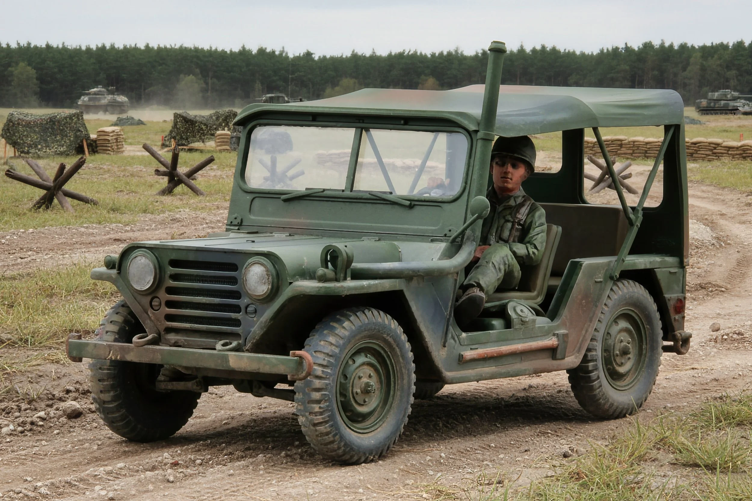 A soldier driving a military jeep across a dirt field during a daytime battle scene with tanks and barbed wire in the background.