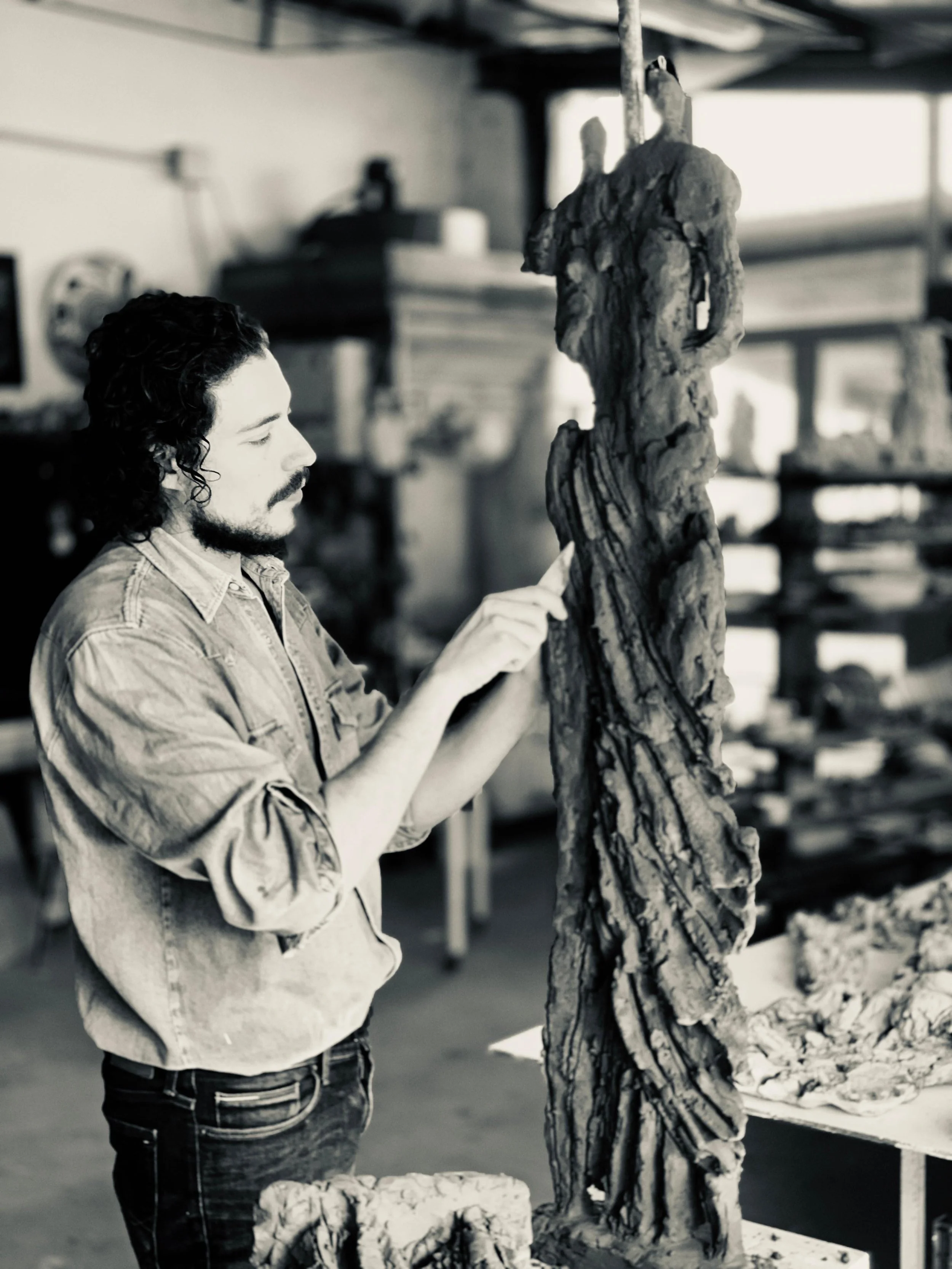 Un uomo con capelli ricci e barba che lavora su una scultura di legno in un'officina.