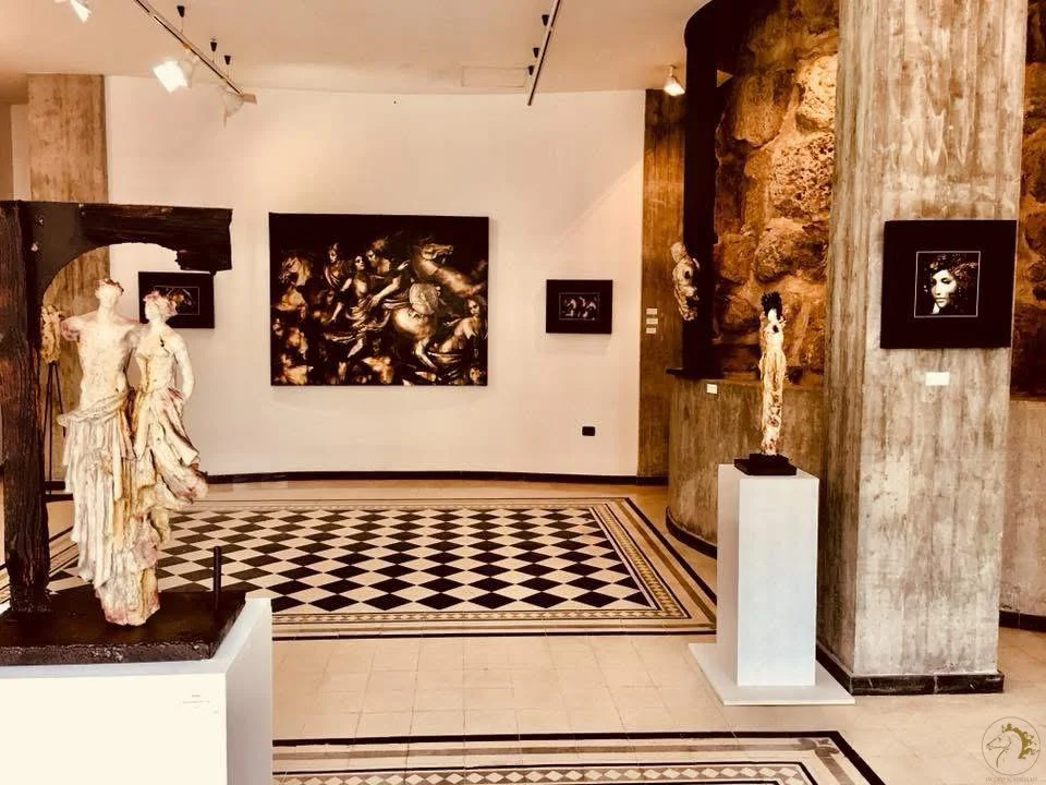 Interno di un museo con sculture e quadri, pavimento a scacchi e pareti in pietra e bianco.