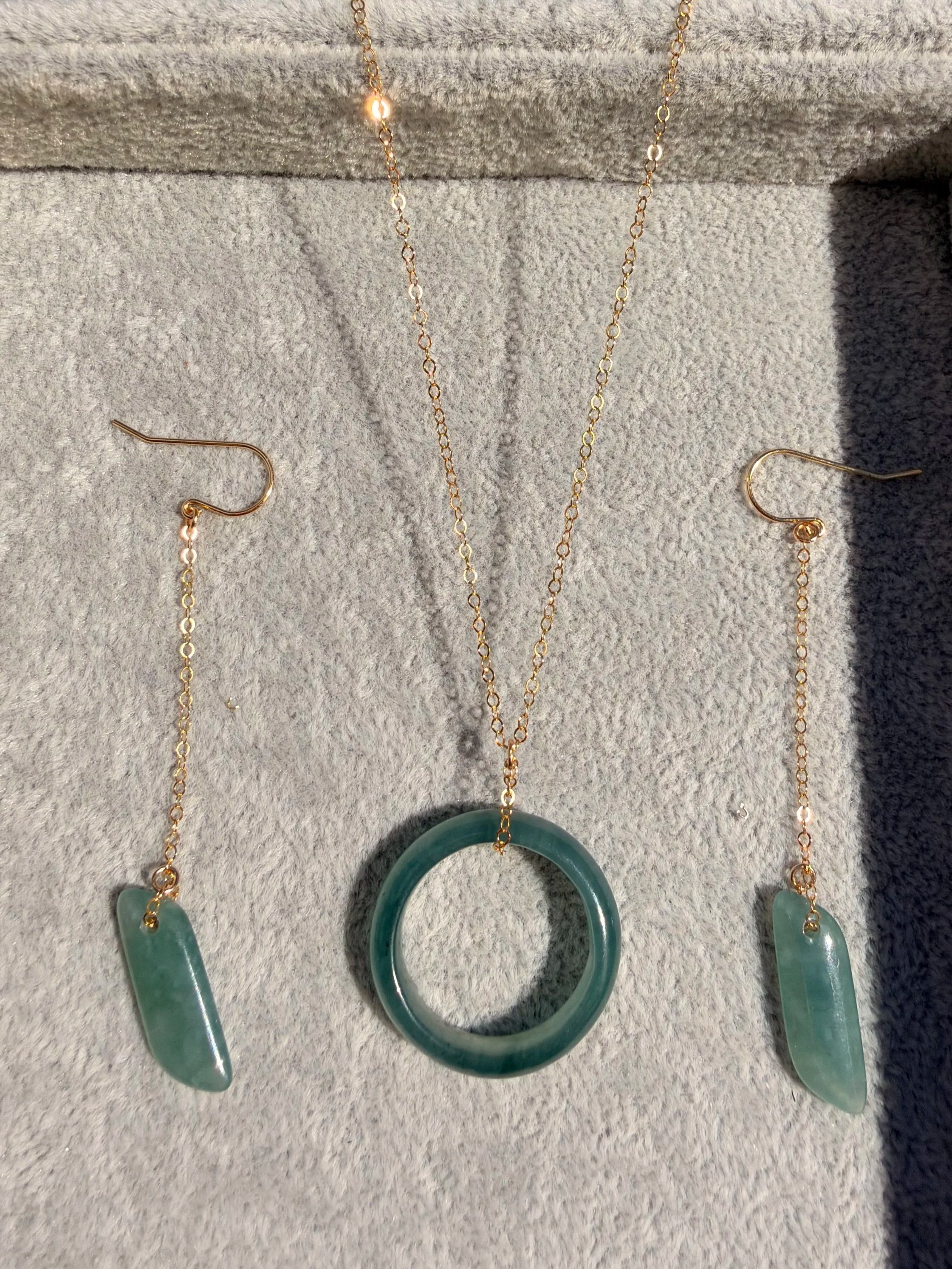 A jewelry set consisting of a gold chain necklace with translucent Type A Jadeite Jadereen circular pendant, and matching earrings with translucent jadeite 
