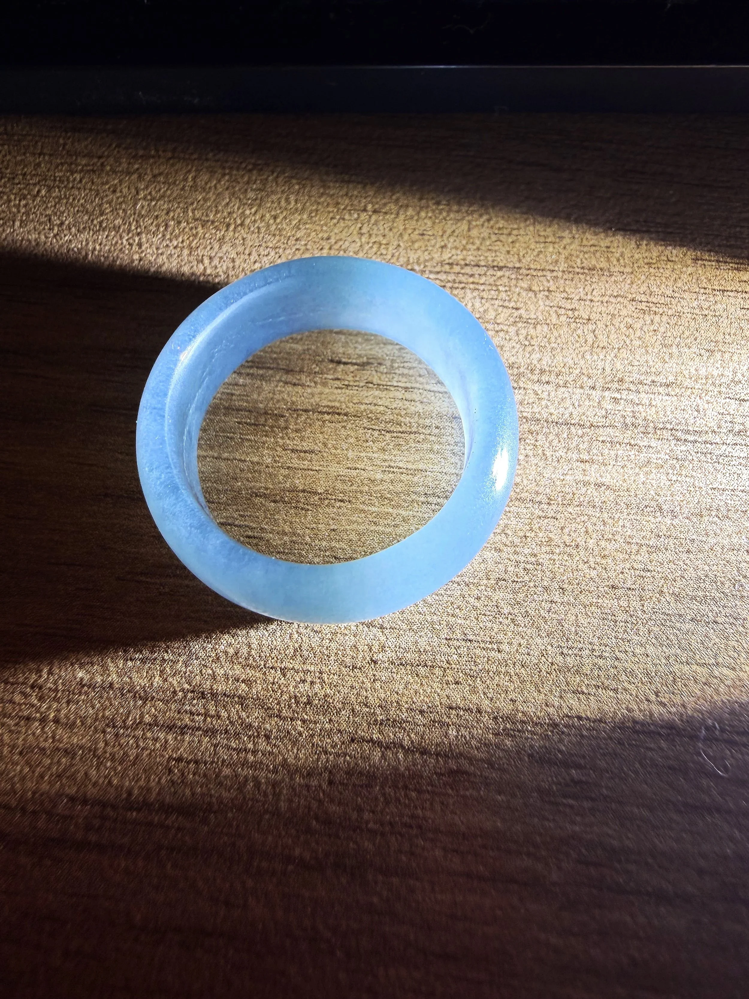 A translucent blue ring resting on a wooden surface with sunlight casting shadow and light patterns.