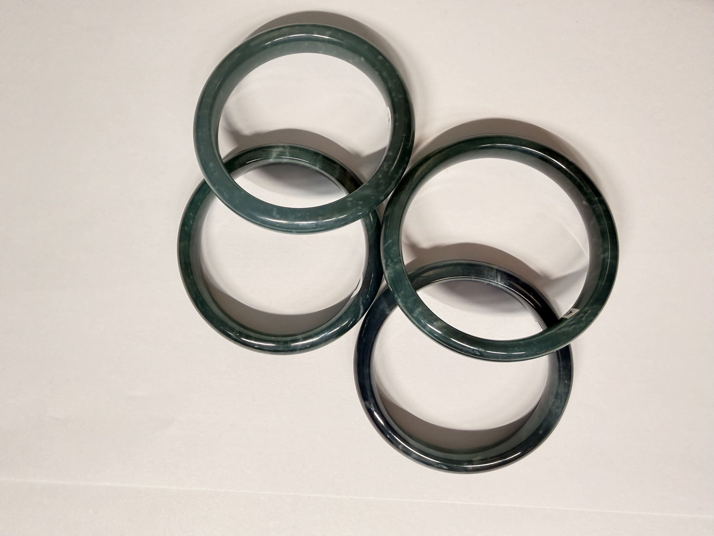 Four beautiful Type A Jadeite Jade bangles sitting on a white surface 