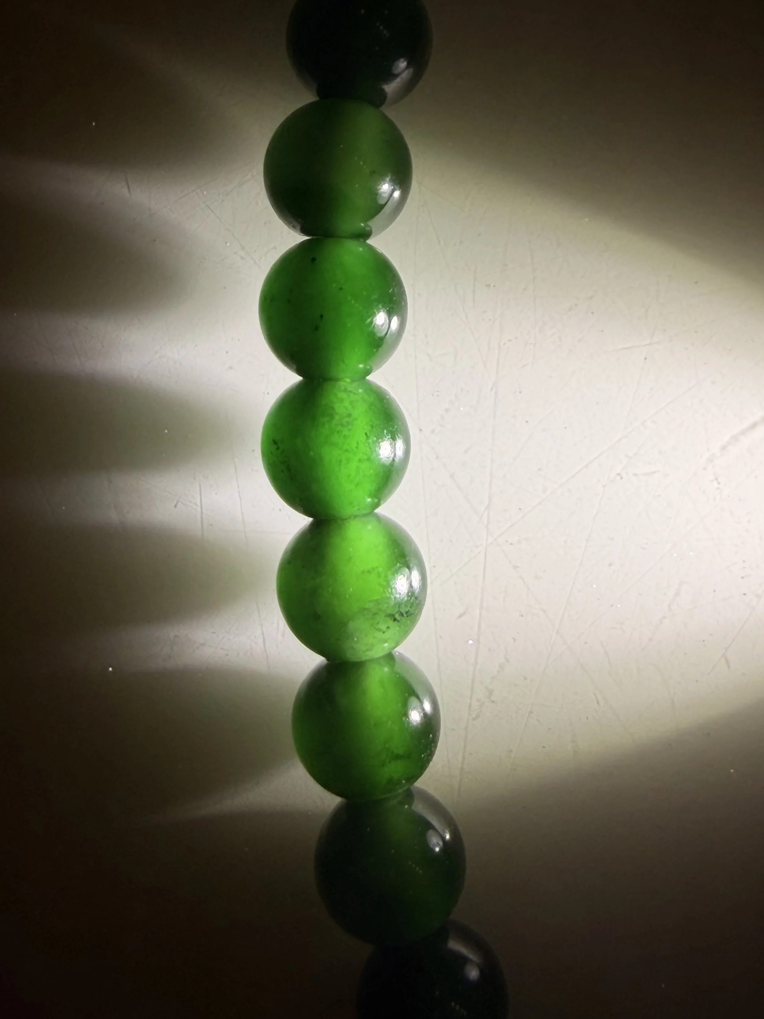 Stacked green jadeite jade spherical beads or balls with light reflecting off them, casting shadows and reflections on the surface below.