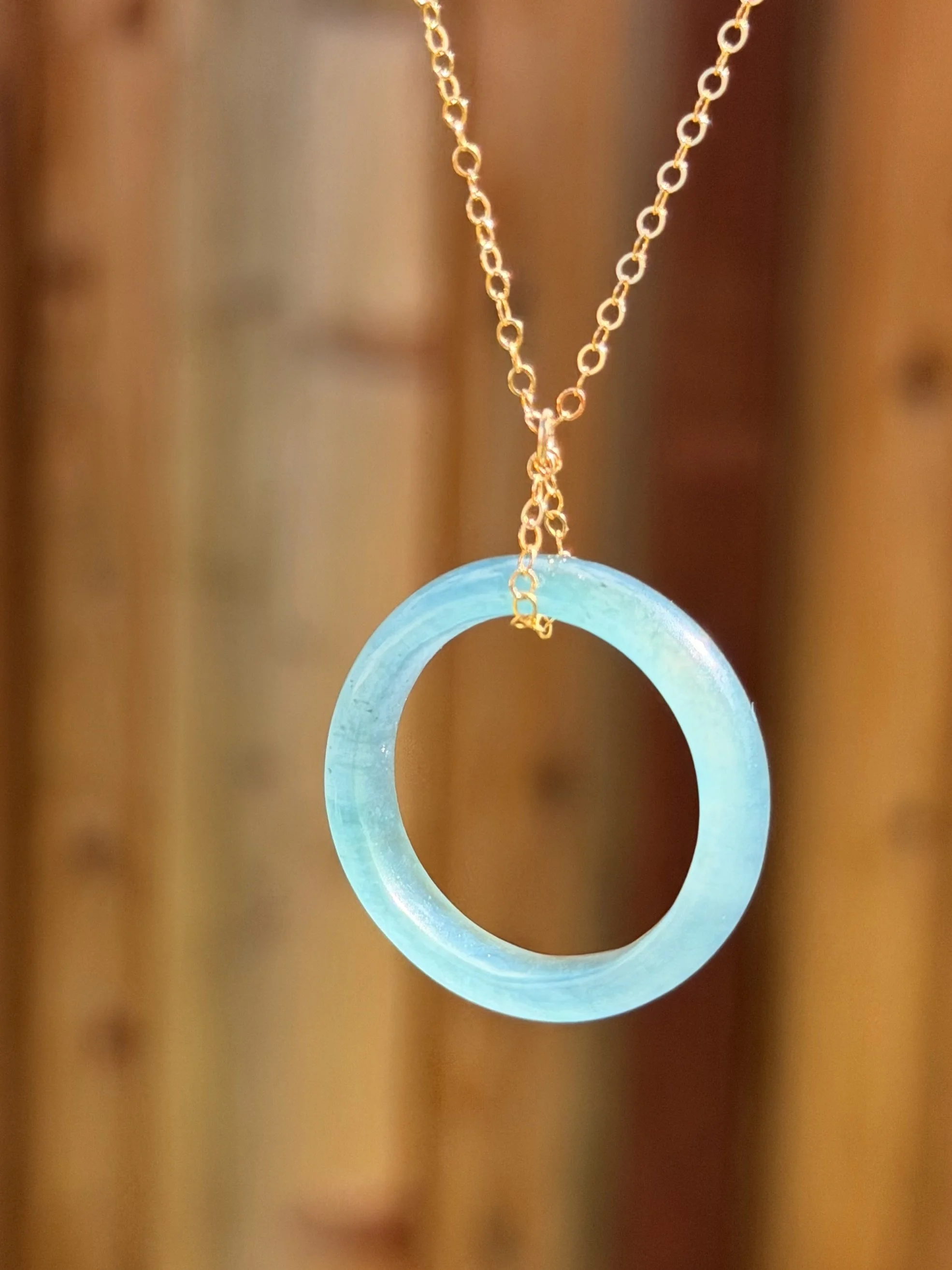 A necklace with a blue jade ring pendant hanging from a gold chain.
