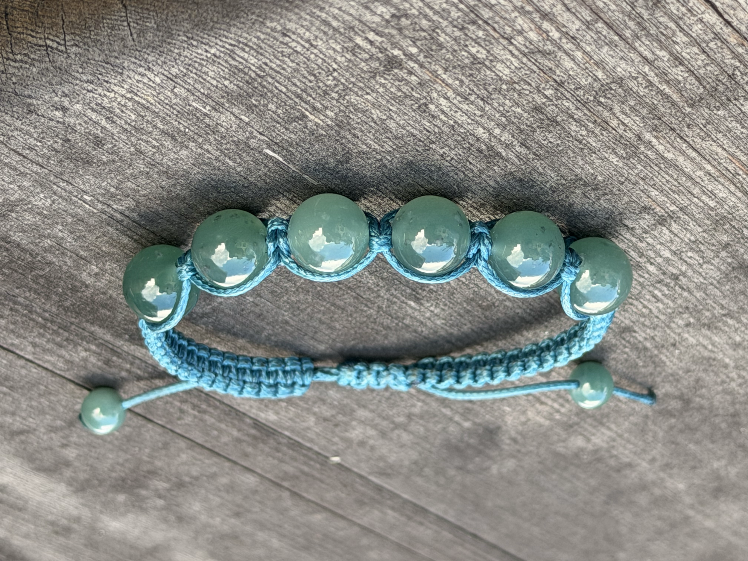 Blue woven bracelet with large light Princesa Green Type A Jadeite Jade beads glowing on a wooden surface