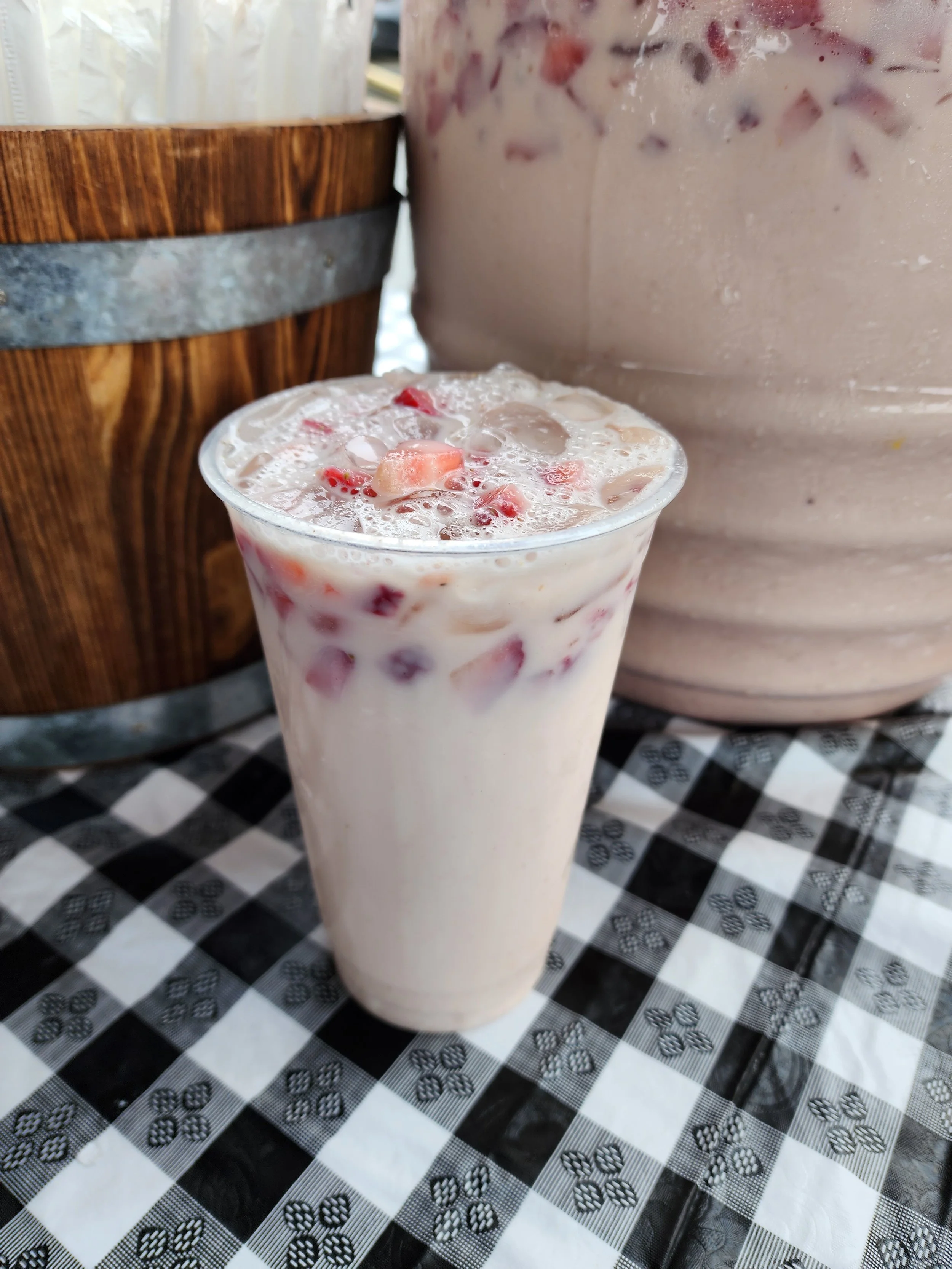A glass of strawberry milkshake with visible pieces of strawberries on top, placed on a black and white checkered tablecloth.