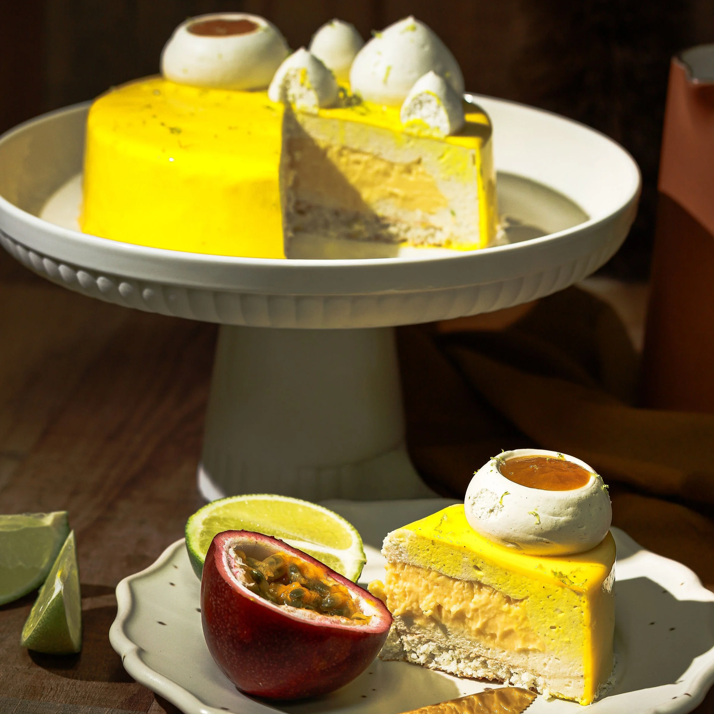 Un gâteau à la lime et à la passion, décoré de panna cotta avec un coulis caramel, présenté sur une assiette avec une moitié de fruit de la passion et un quartier de citron vert.