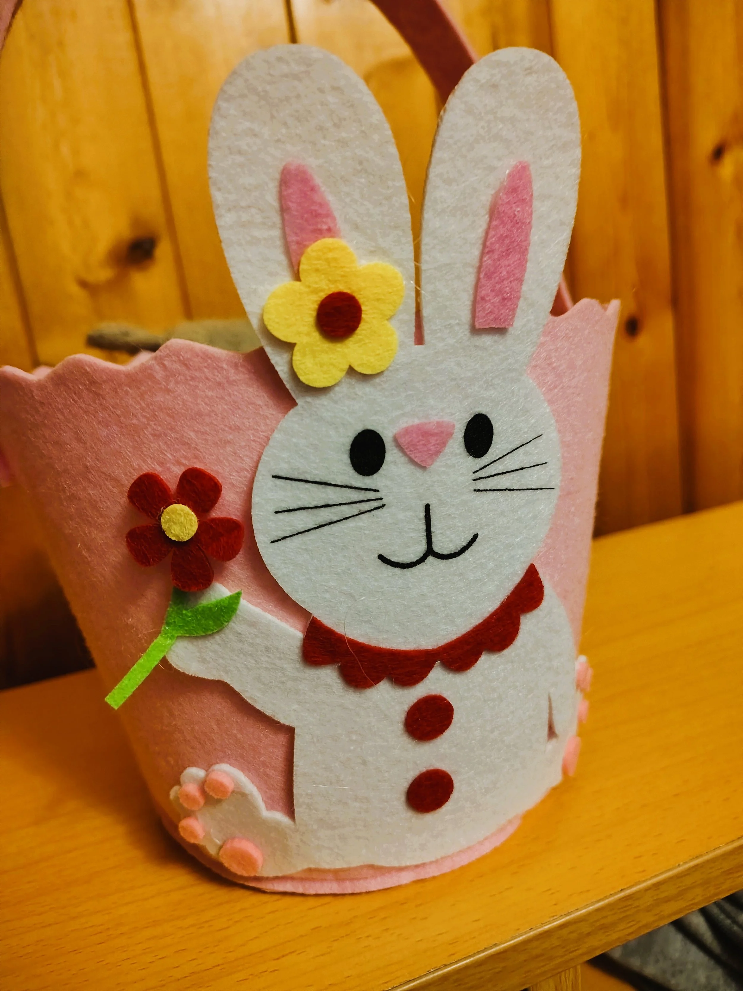 Felt Easter Bunny decoration with pink, white, yellow, brown, green, and black felt details, featuring a bunny holding a flower with a wooden background.