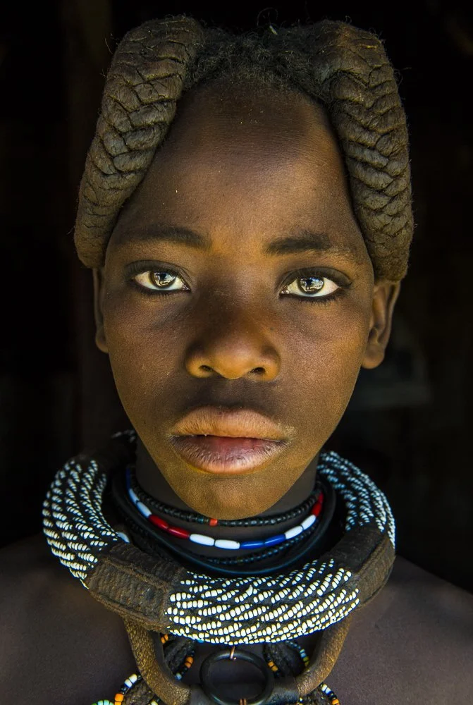 Close-up portrait of an African girl with braided hair, wearing traditional beaded necklaces.