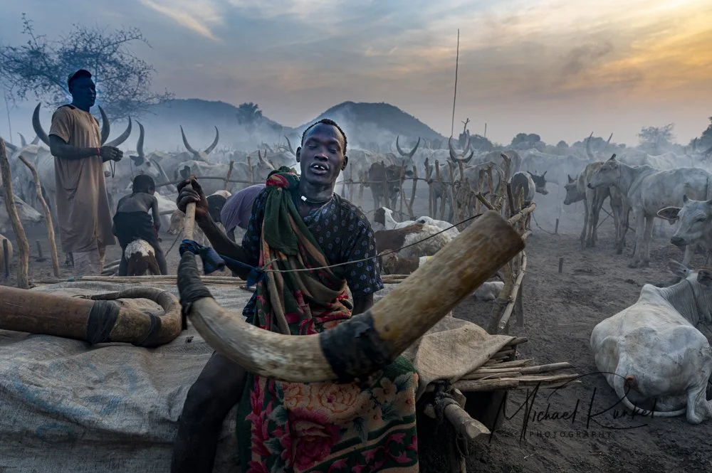 A Mundari tribe man playing a cow-horn trumpet, or tung, of their revered revered Ankole-Watusi cattle, South Sudan, Africa.