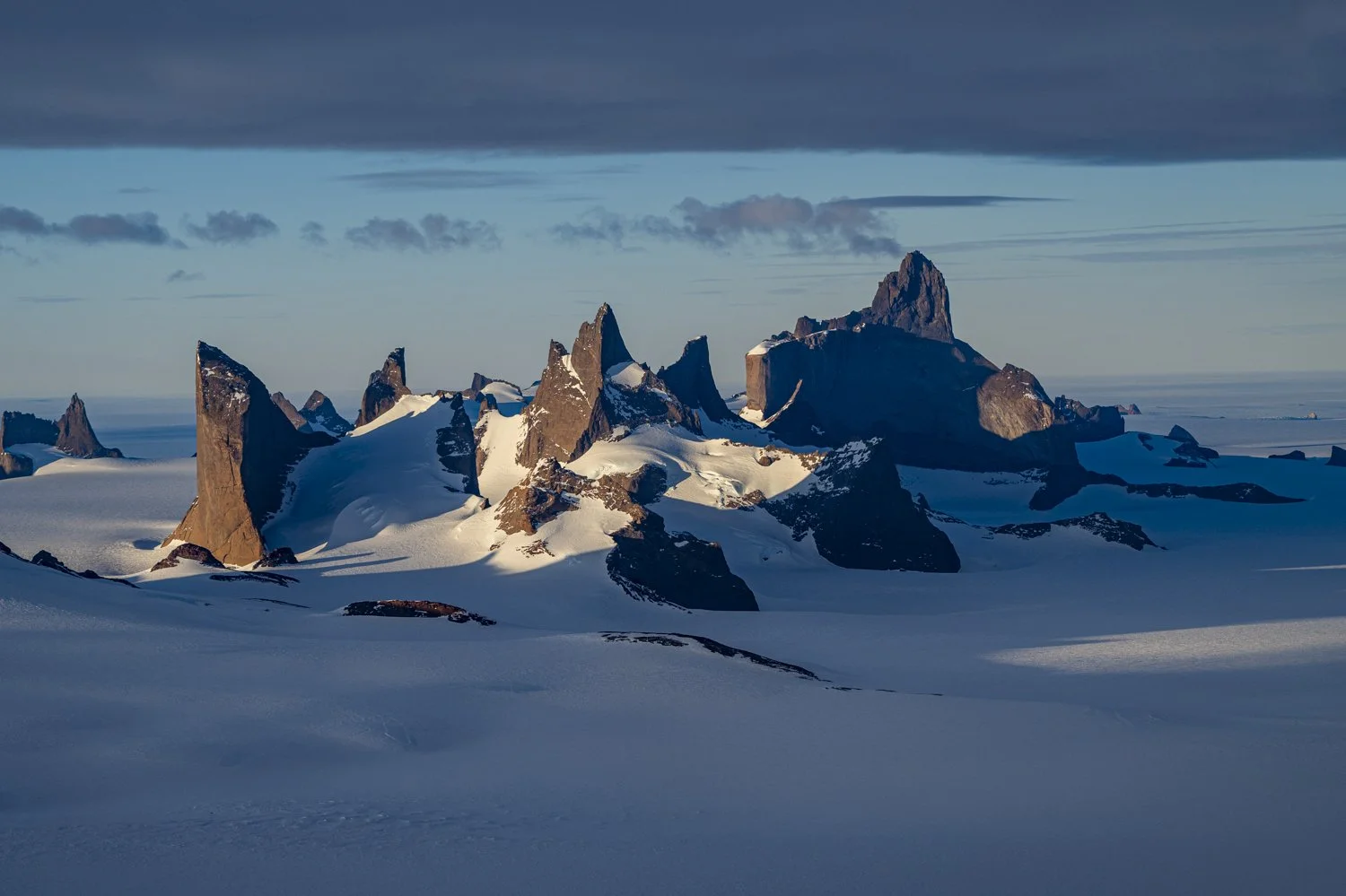 Snow-covered rocky mountain peaks under a cloudy sky.
