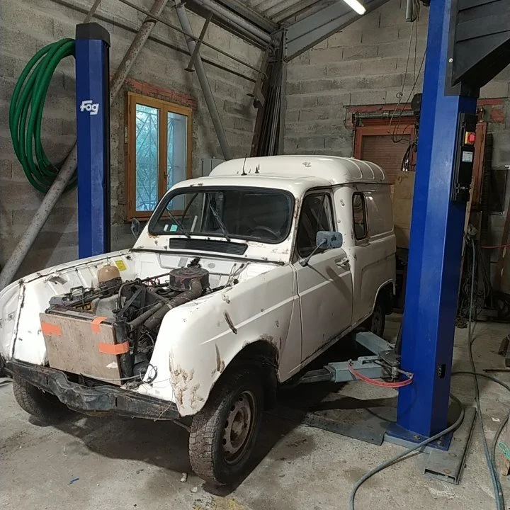 Voiture ancienne en réparation dans un garage, sans capot moteur, partiellement disassemblée.