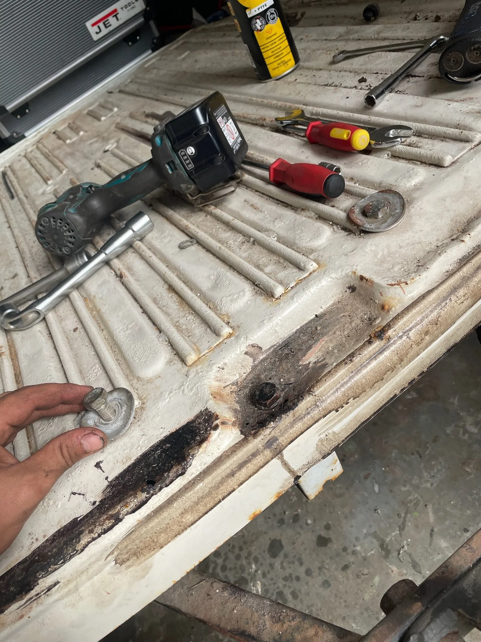 Outils de réparation disposés sur une surface en métal, dont une perceuse sans fil, un tournevis, un pince, une clé à molette, un détendeur de gaz, une pièce en métal, et une main tenant une vis.