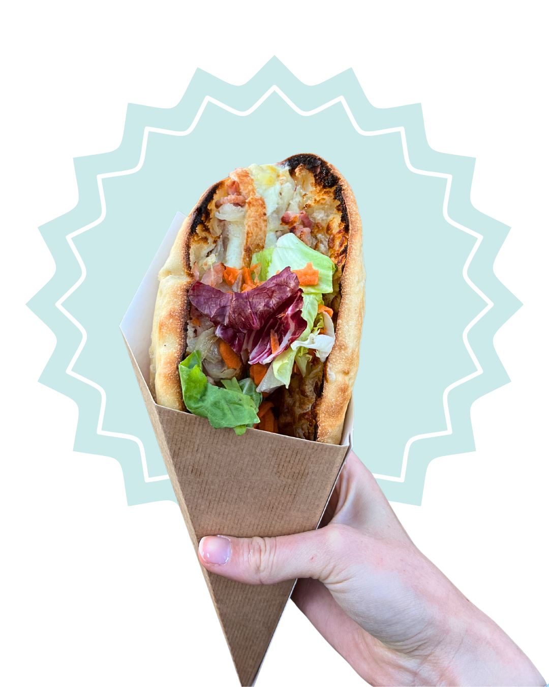 Faluche avec salade, tranches de tomate, carottes, et une sauce, dans un emballage en papier, tenu par une main.