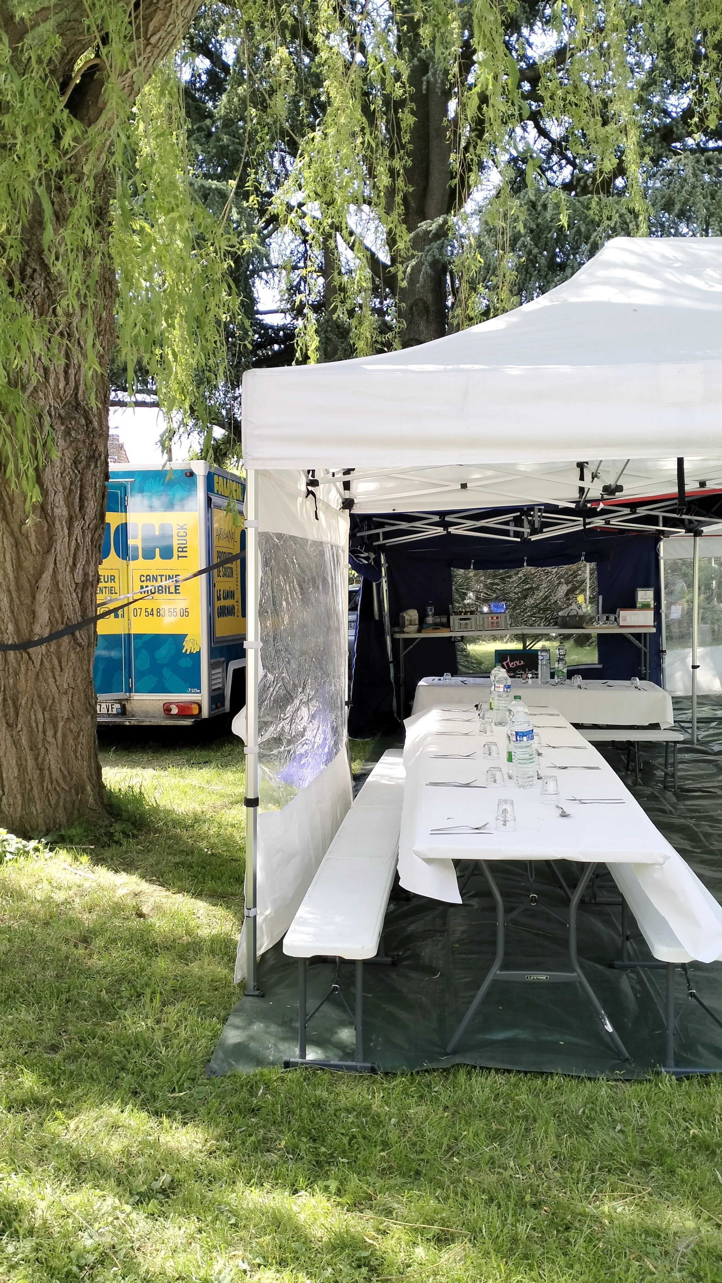 Barnum et installation pour un repas en extérieur, organisé par Faluch'Truck à côté d'un arbre.