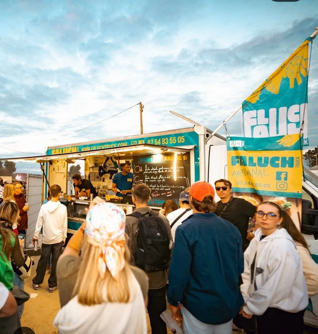 Une foule de personnes devant le Faluch'truck avec un logo et un menu affichés, en plein air sous un ciel partiellement nuageux.