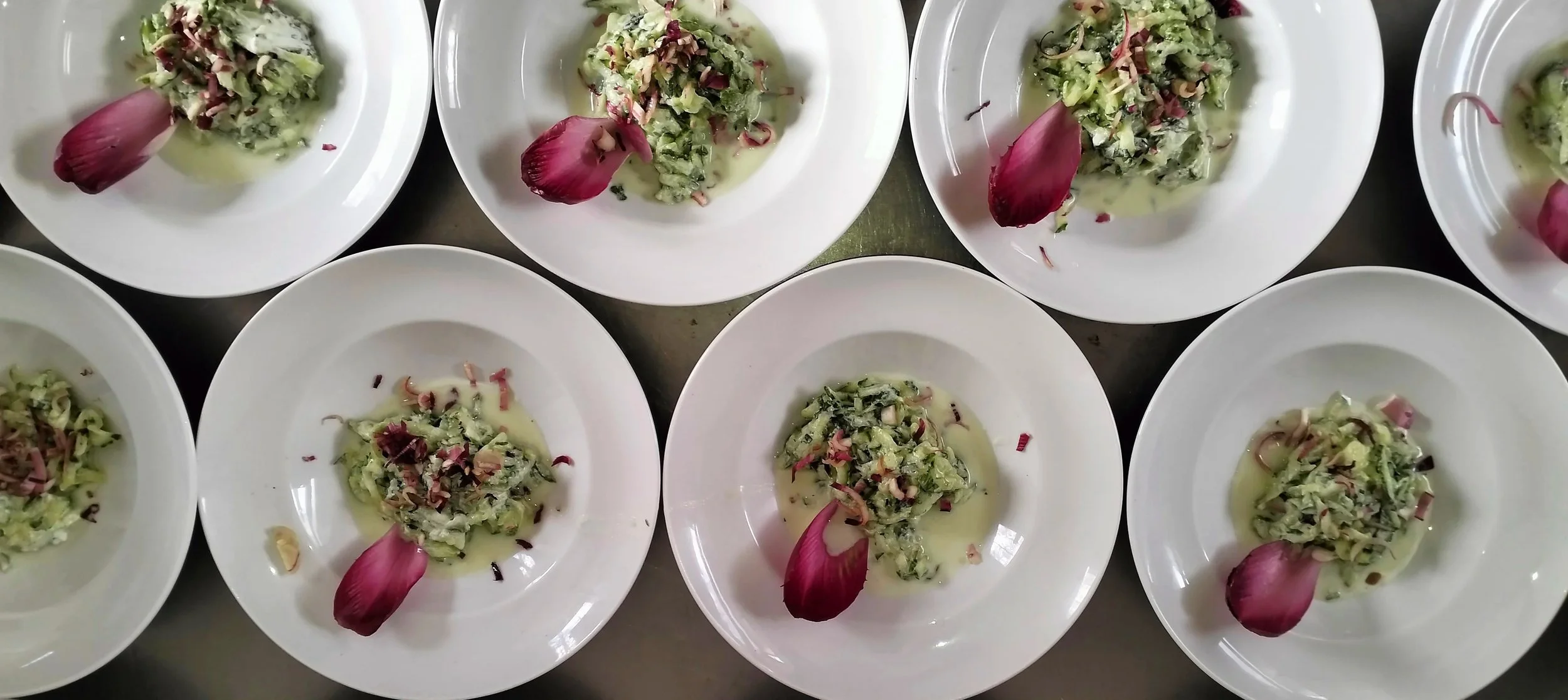 Des assiettes blanches contenant une salade verte agrémentée de morceaux de viande ou de jambon, garnies de pétales de rose rouge vif.