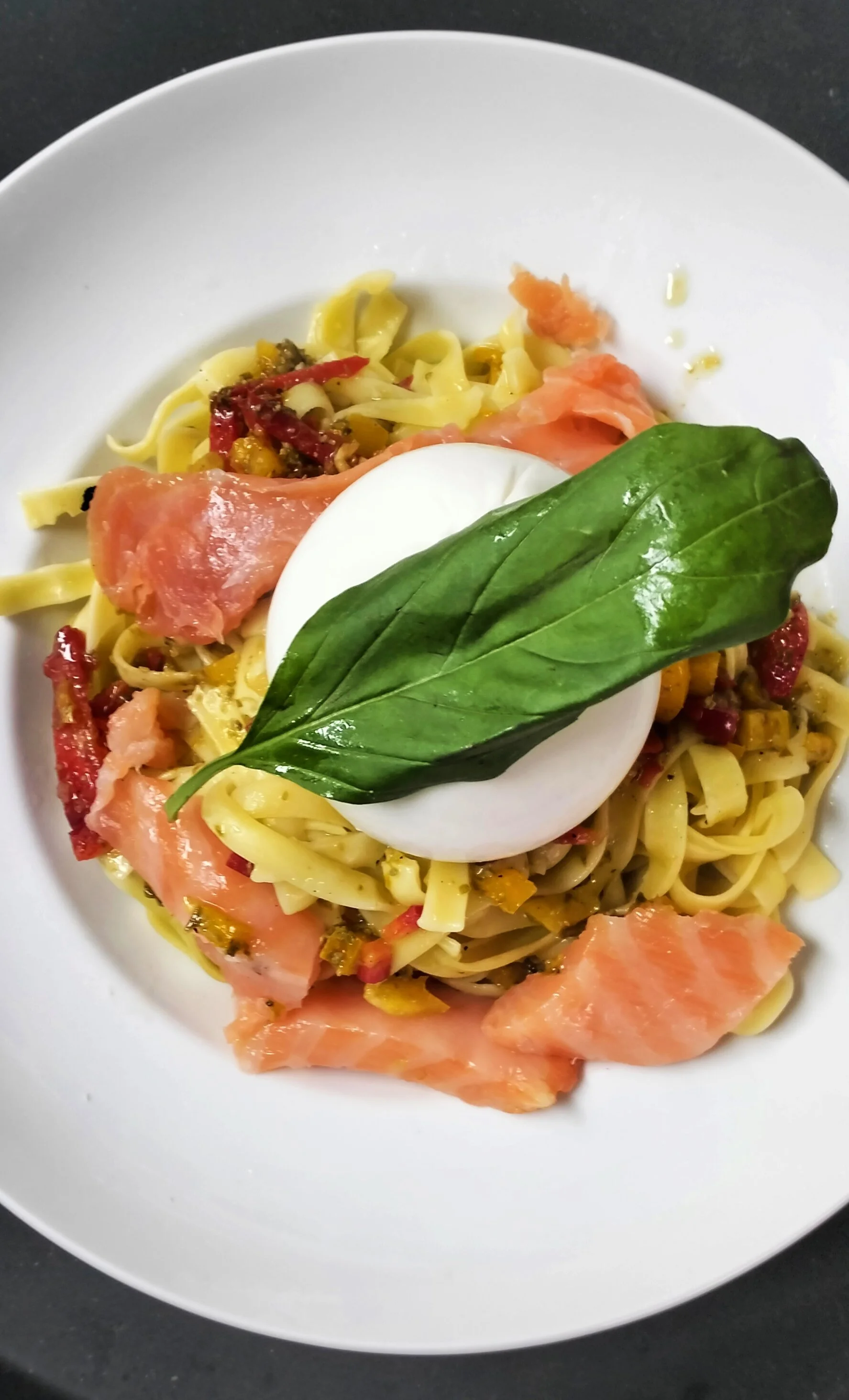 Assiette de pâtes with prosciutto, un œuf mollet, une feuille de basilic et des morceaux de tomate séchée.