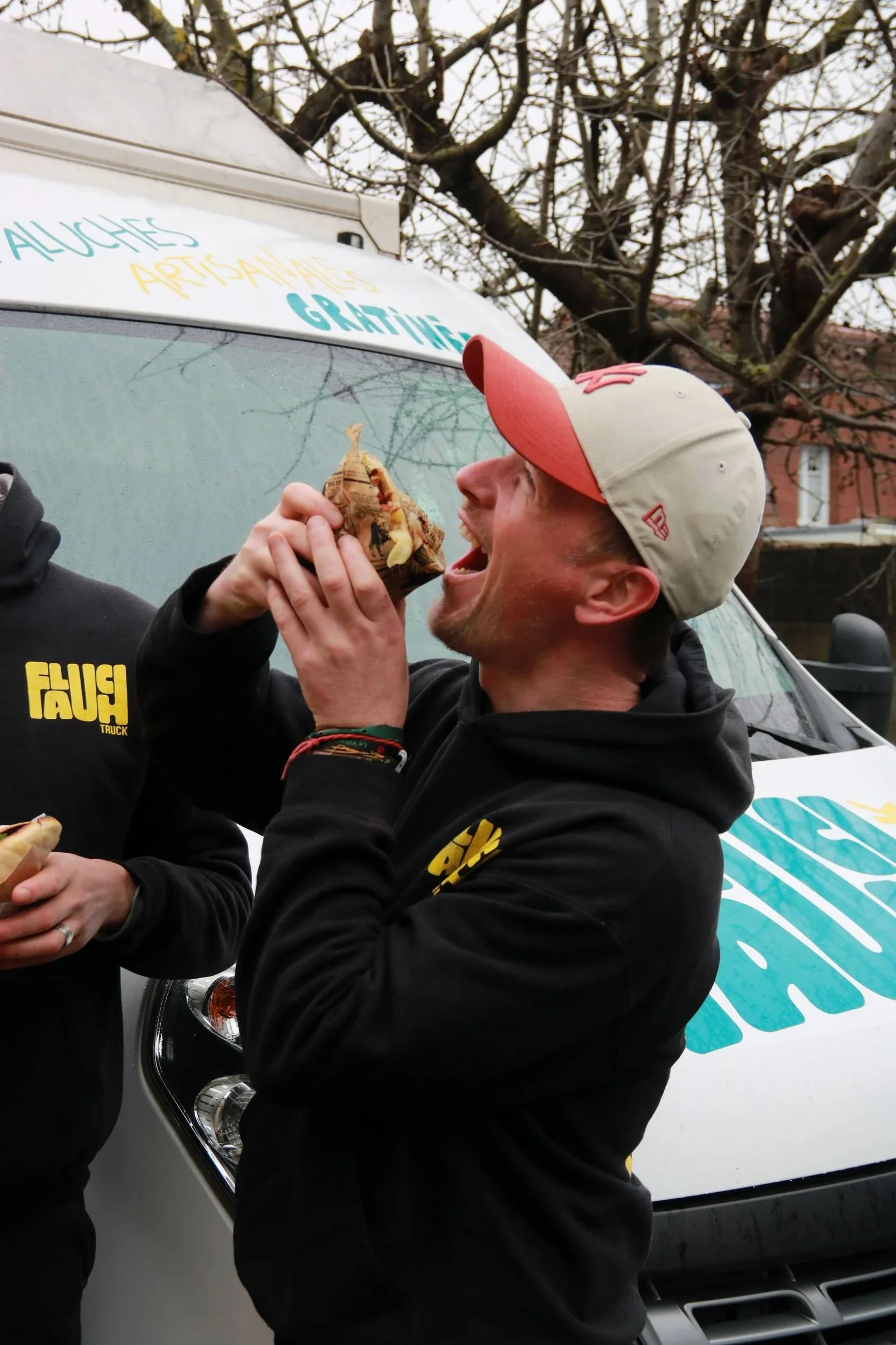 Un homme qui mange une faluche à l'extérieur avec un véhicule en arrière-plan.