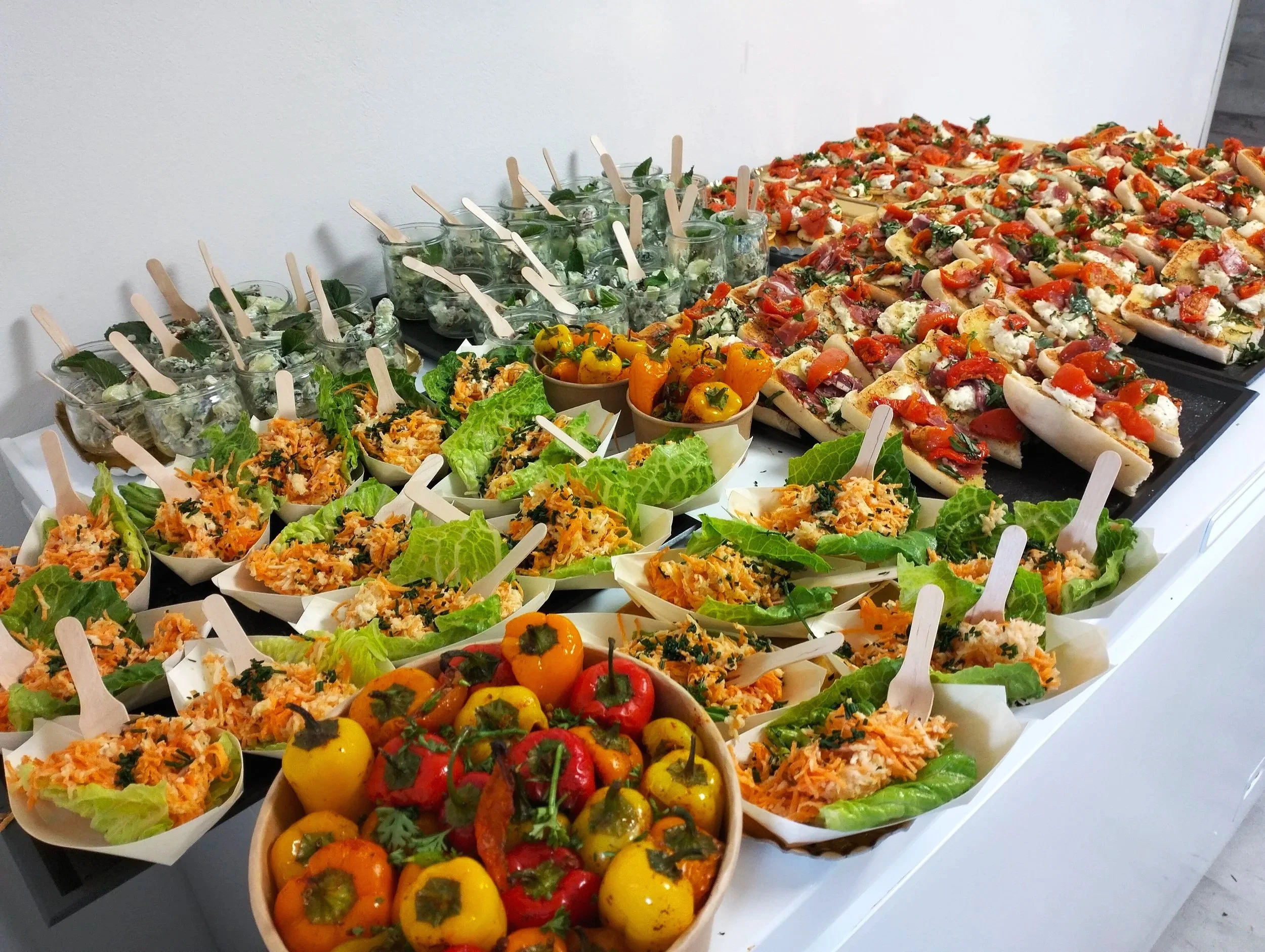 Buffet : plateau de hors-d'œuvres avec des petits piments colorés, des verrines avec des salades et des mini pizzas garnies de tomates, fromages et herbes. Beaucoup de petits morceaux de légumes et de recettes variées.