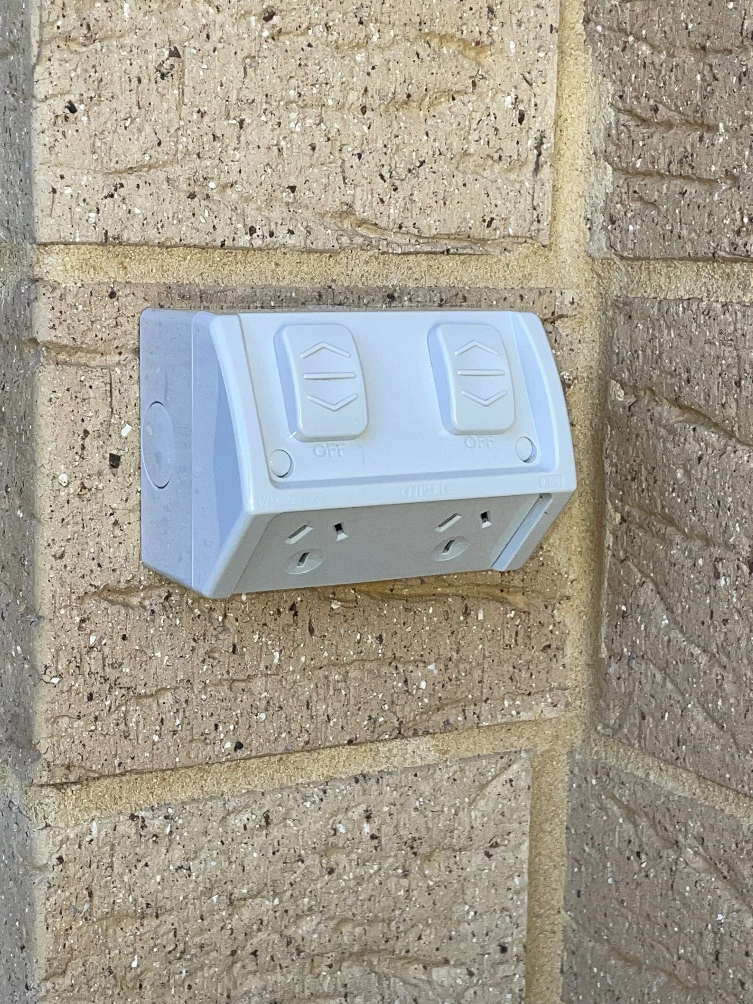 White outdoor electrical outlet box with two switches mounted on a brick wall.