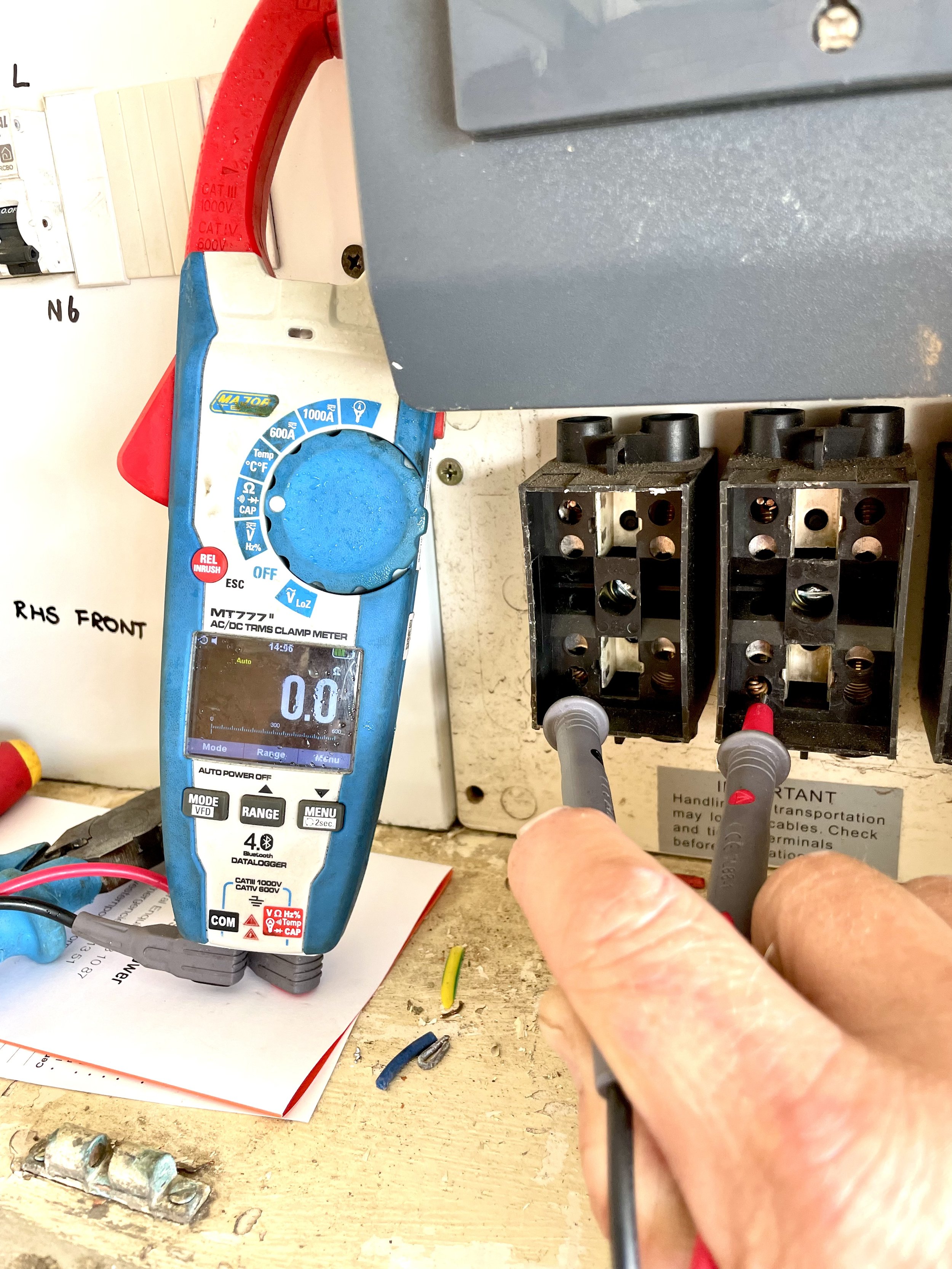 A person using a multimeter to test an electrical connection or component in an electrical panel enclosures with black terminal blocks, wires, and labels.