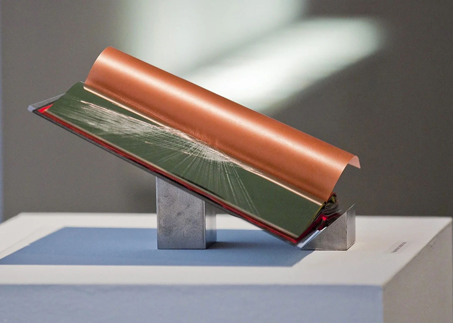  Installation shot showing the book on the hand made book stand that is an integral part of the work. Bookstand: 12″ x 12″ clear plexiglass, laid on handmade, hand-polished steel columns made of rough discarded construction steel hand sanded and hand