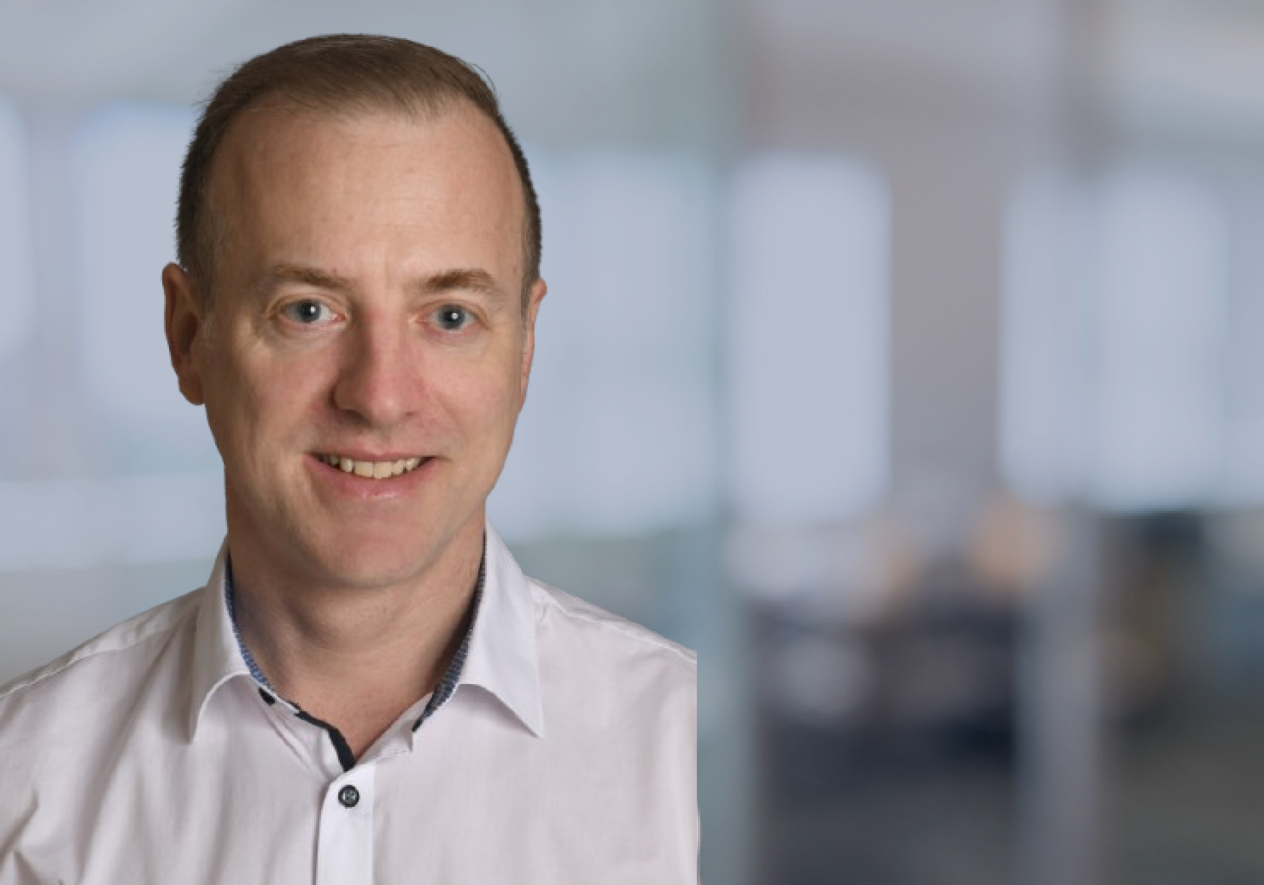 Jürgen Schultz in einem weißen Hemd, im Hintergrund eine moderne Bürolandschaft.