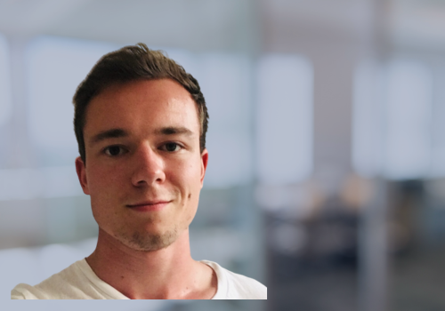 Marvin Bilharz, Web Developer mit dunklen Haaren vor einem modernen Bürohintergrund.