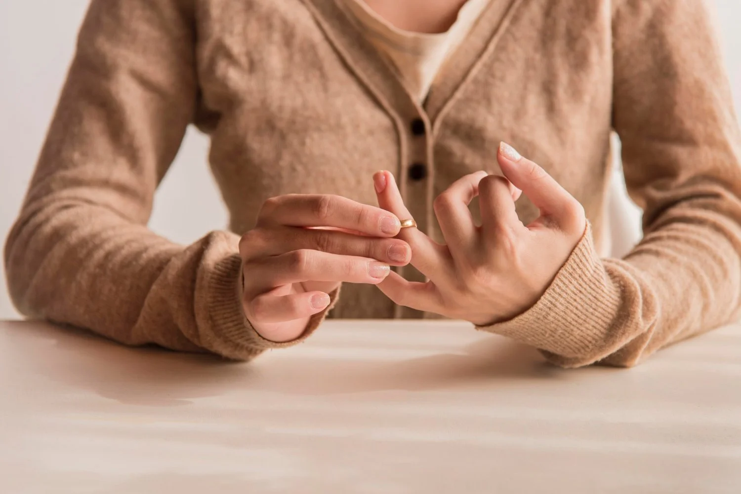 Person wearing a beige cardigan placing a ring on their finger over a light-colored table.
