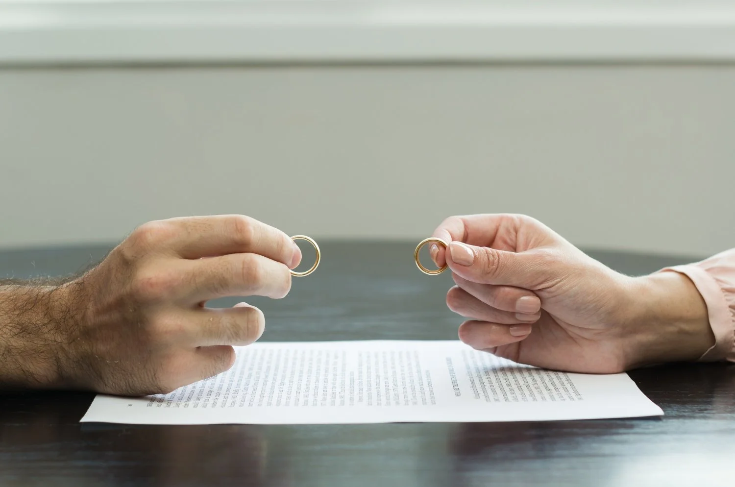 Two people exchanging wedding rings over a document on a dark table.