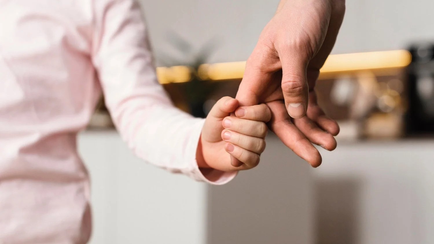 A child holding an adult's finger in a gentle, caring manner.