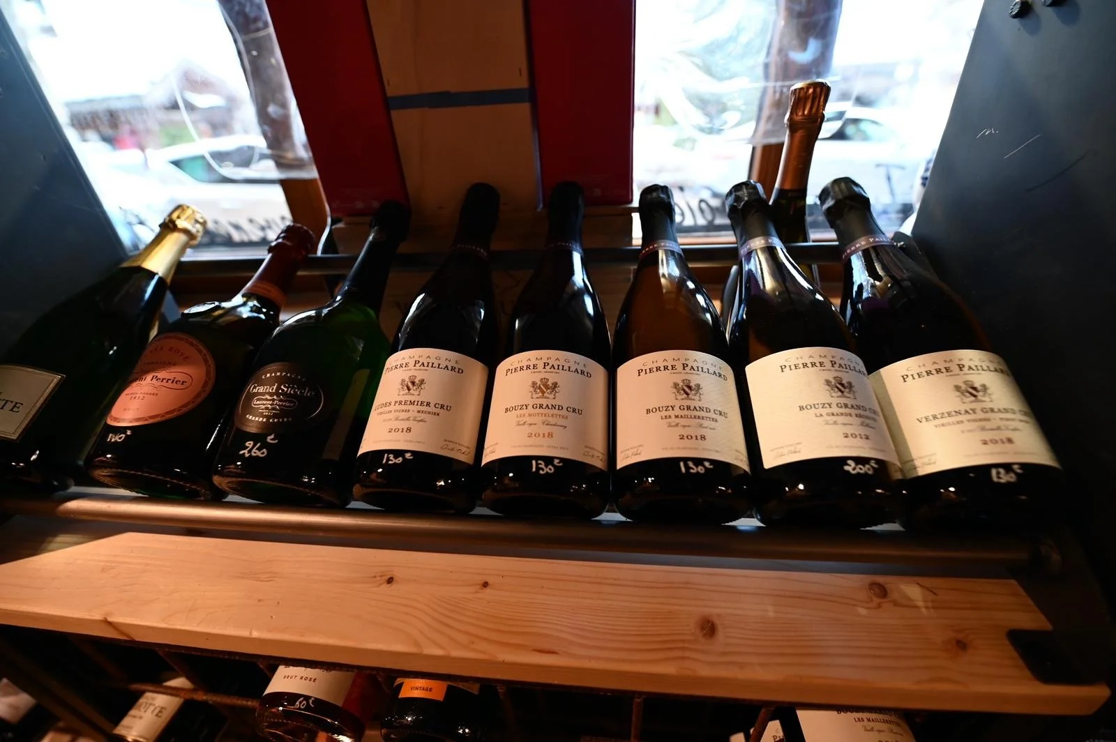 Une rangée de bouteilles de champagne alignées sur une étagère en bois près d'une fenêtre