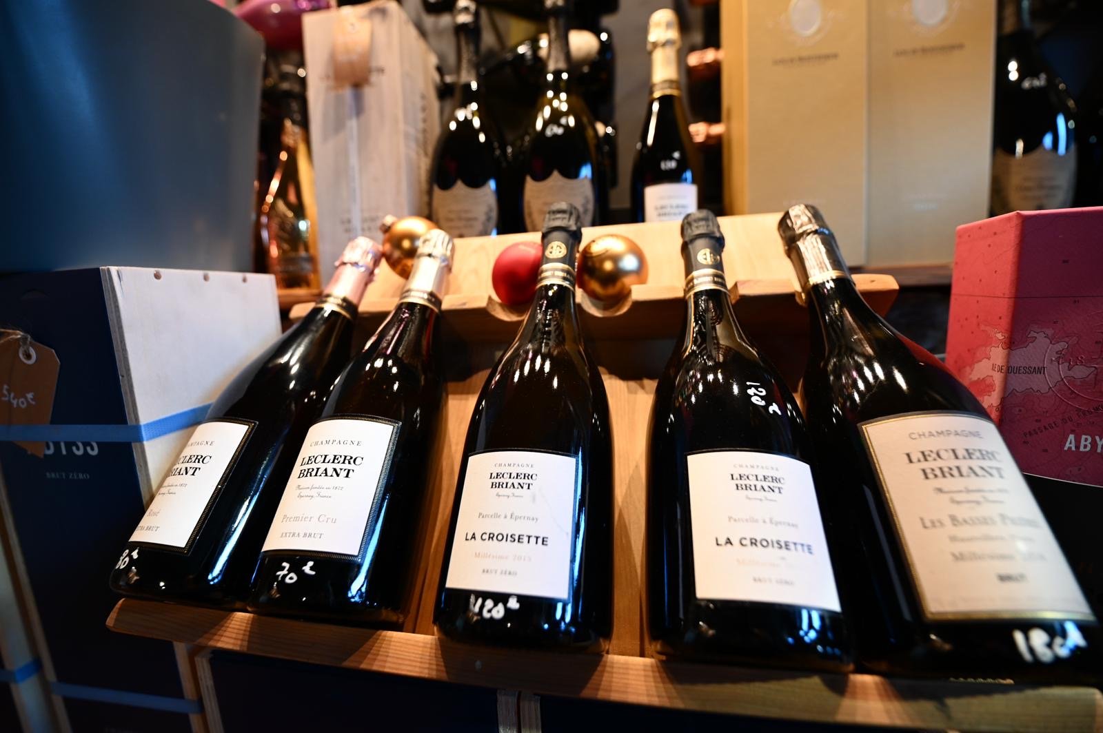 Cinq bouteilles de champagne Leclerc Briant alignées sur une étagère en bois, avec des décorations dorées et rouges sur le dessus.