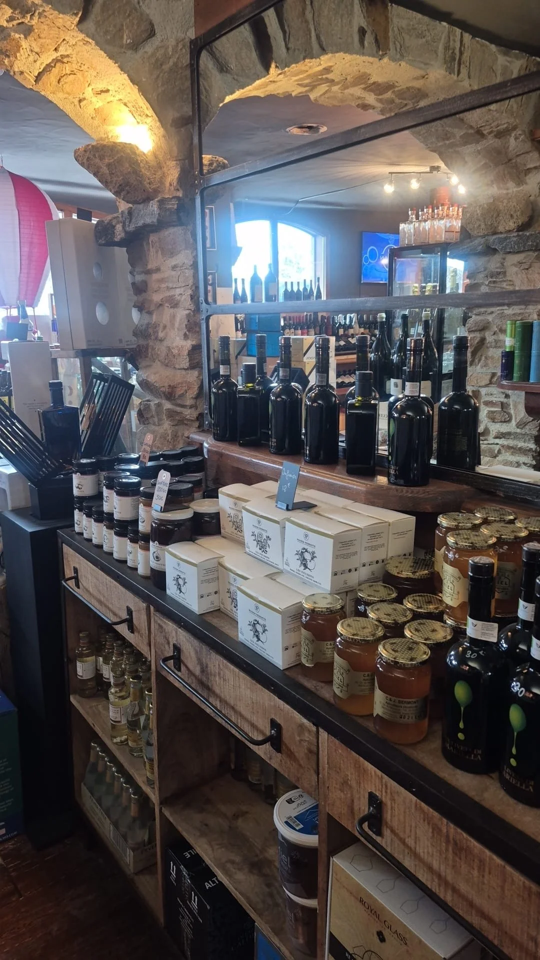 Étagère dans un magasin alimentaire avec des bouteilles de vin, des bocaux de miel, des boîtes et des petits flacons.