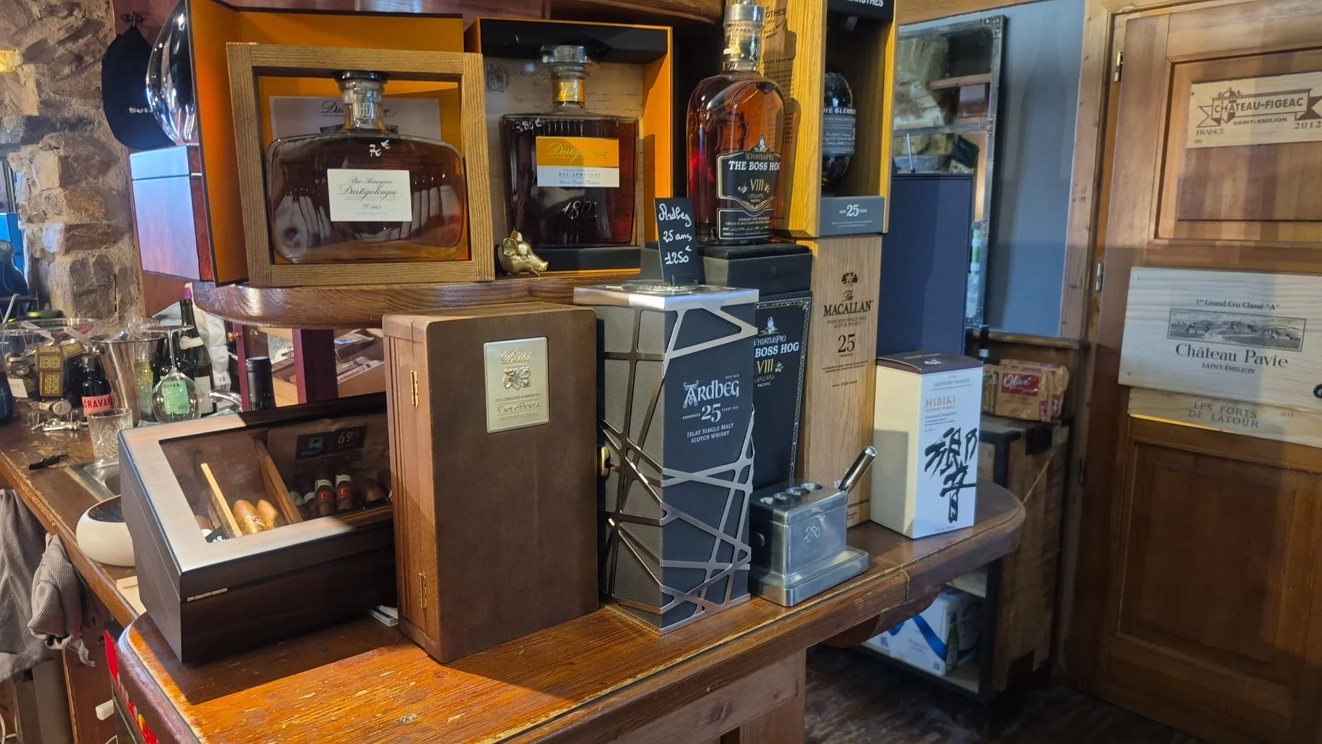 Étagère en bois avec plusieurs bouteilles de whisky, un coffre à cigares, une boîte à souvenirs et différents objets décoratifs dans un intérieur en bois.