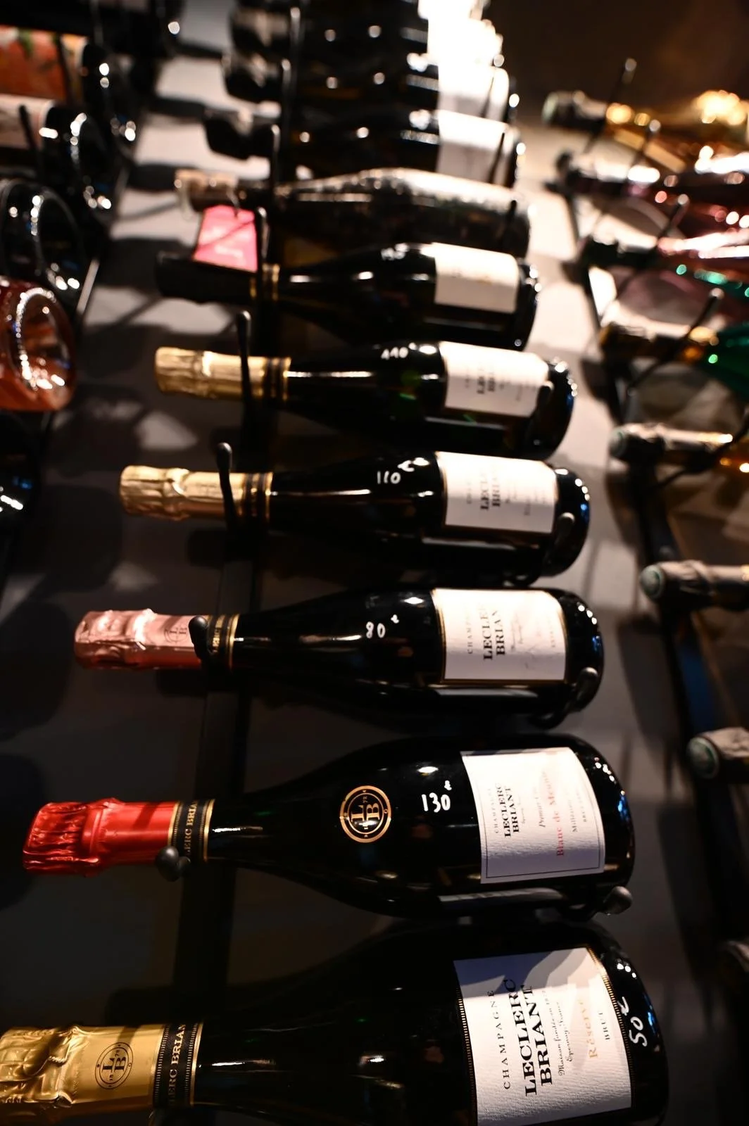 Vues de plusieurs bouteilles de champagne alignées sur une surface, certaines avec un étiquetage visible, conservées dans des racks ou supports.