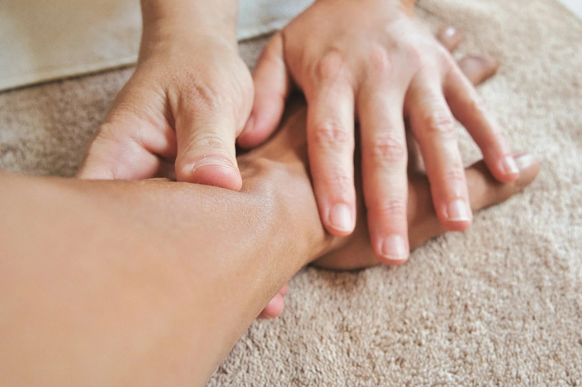 A person is giving a massage to a child's arm on a soft beige surface.