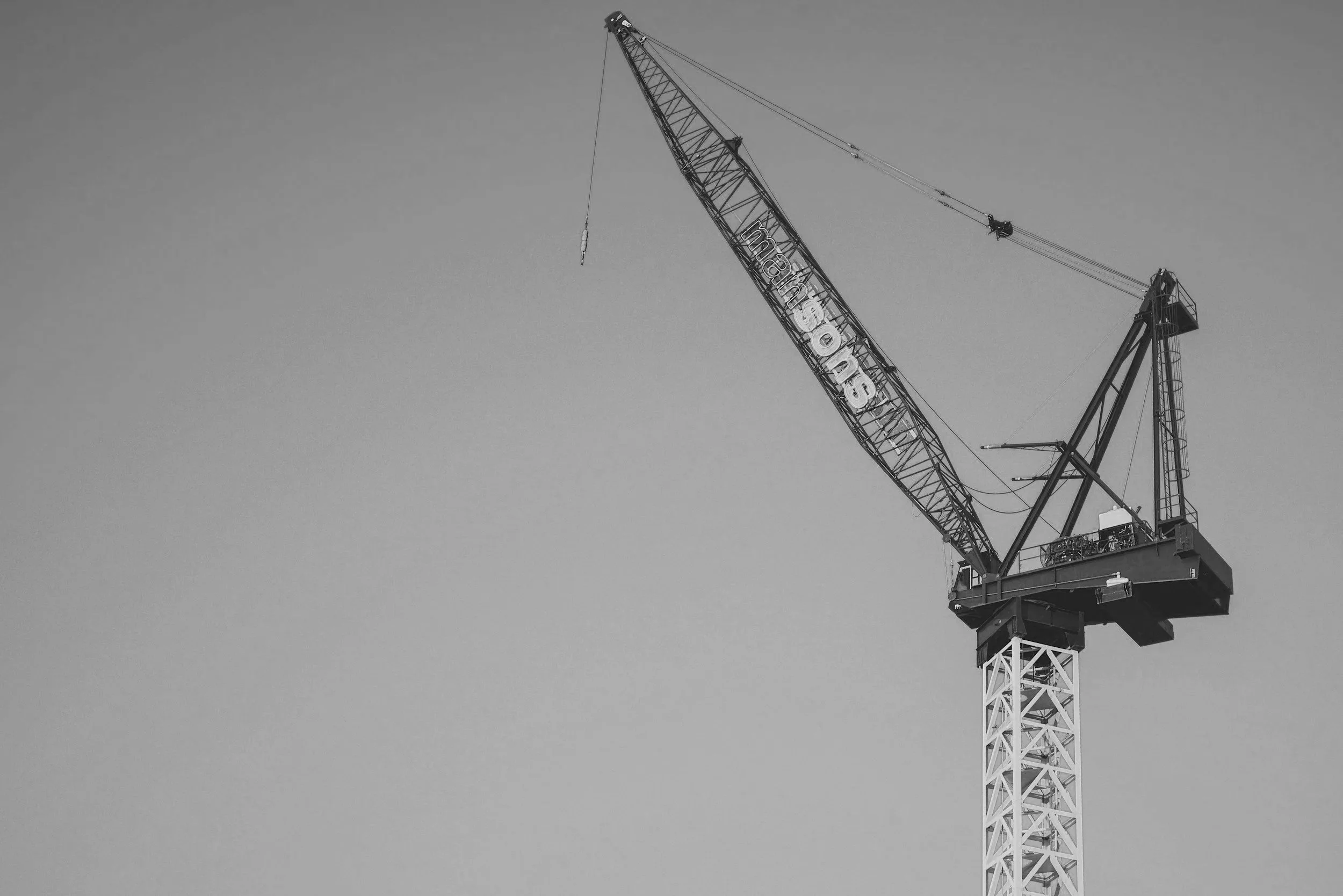 A large construction crane with a lattice tower and a long boom extended upward, set against a clear sky.