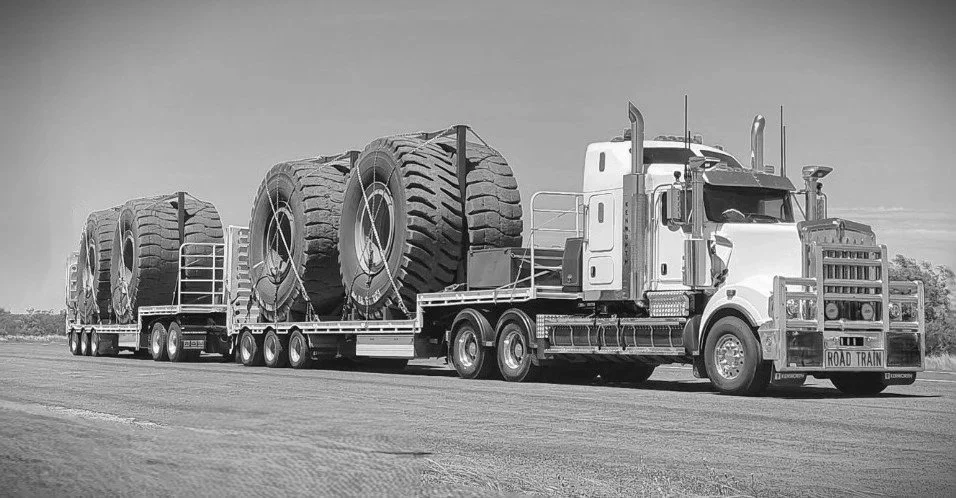 A large semi-truck with a flatbed trailer transporting oversized tires on an open road.