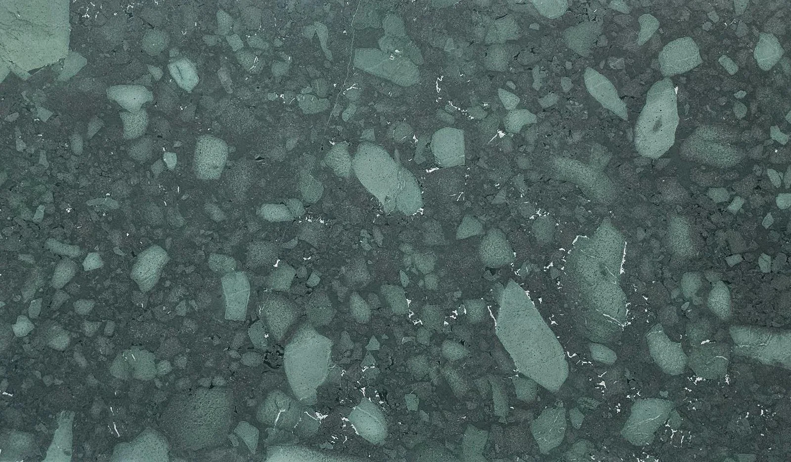 Close-up of a dark stone or asphalt surface with small and medium-sized rocks embedded.