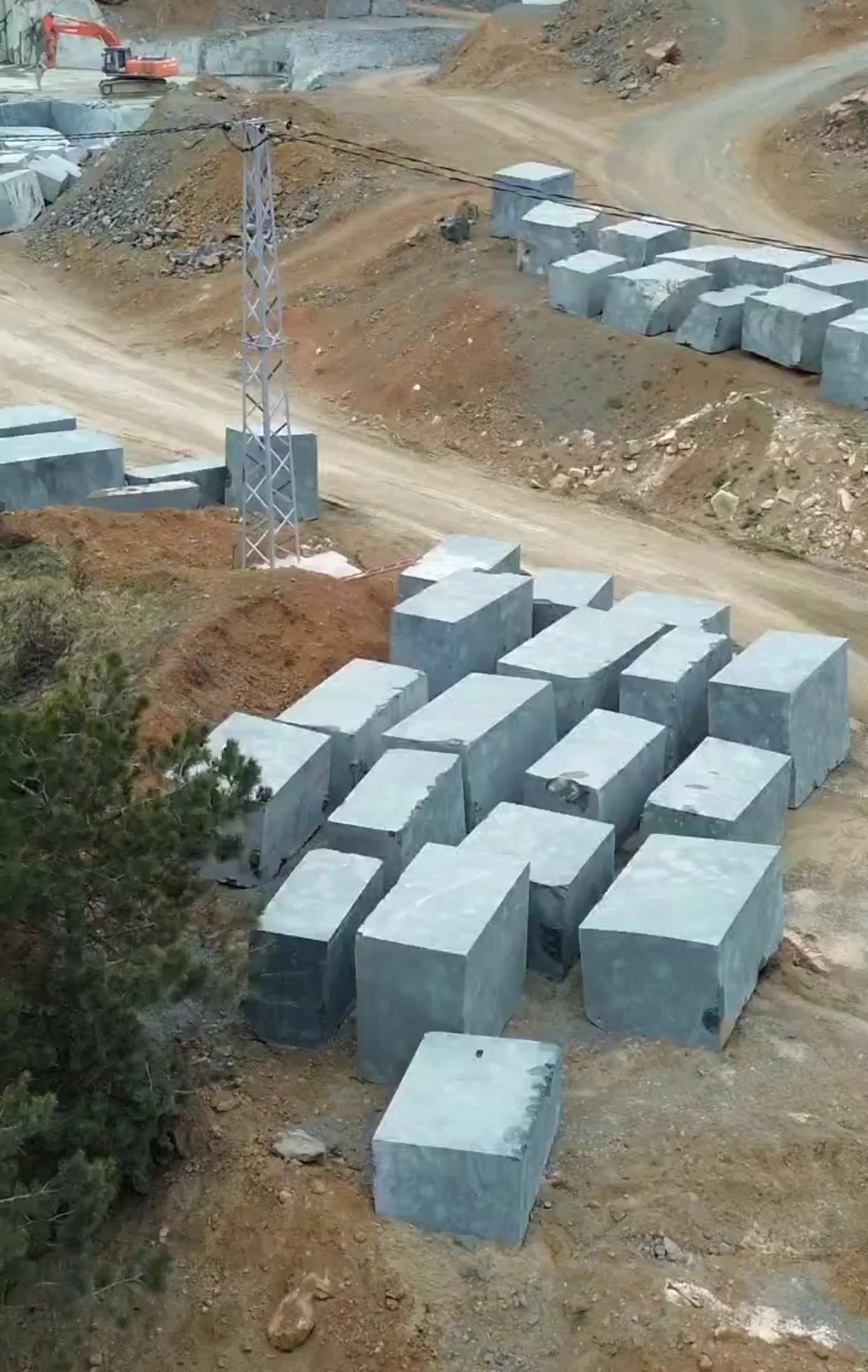 Large concrete blocks at a construction site on a dirt road with hills and construction equipment in the background.