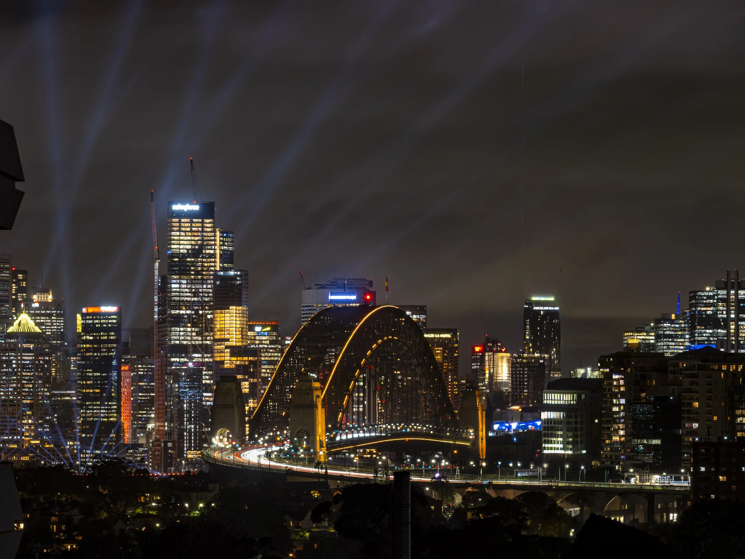 Nighttime city skyline with illuminated skyscrapers, bridges, and light beams, showing a modern urban area.