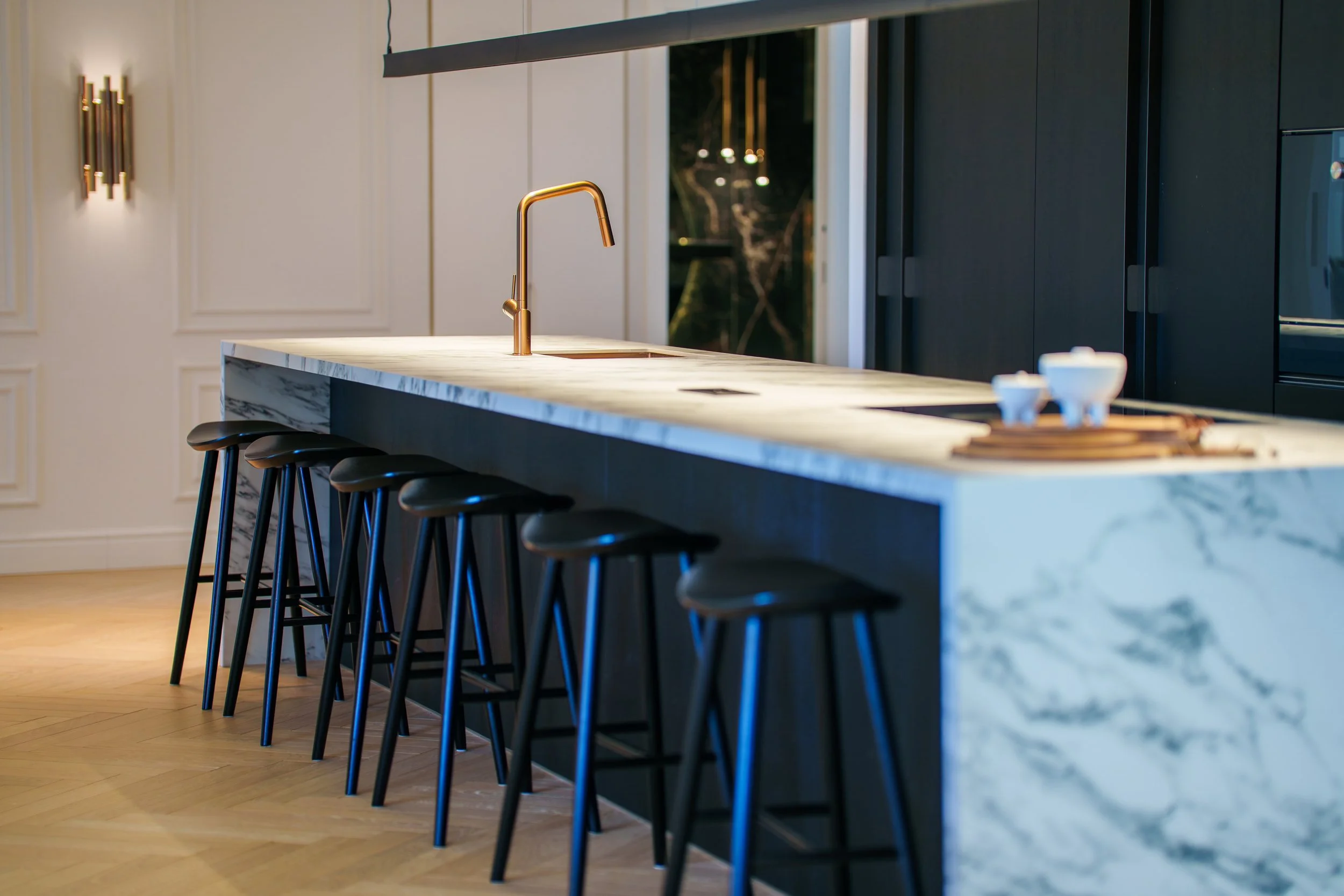 Close-up of the marble breakfast bar with high-end gold fixtures and views into the open-concept living space.