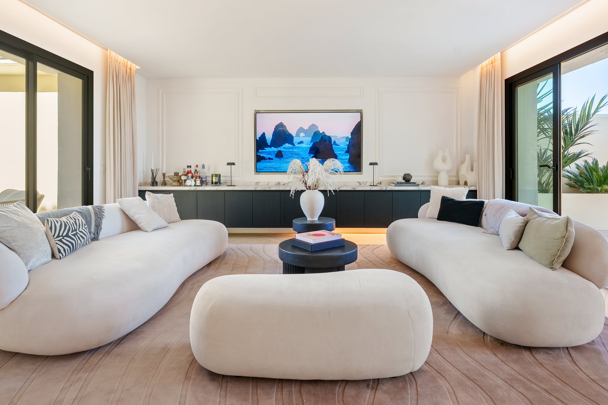 Bright, open-plan living room with curved Scandinavian-style sofas, light oak herringbone flooring, and large windows leading to the terrace.