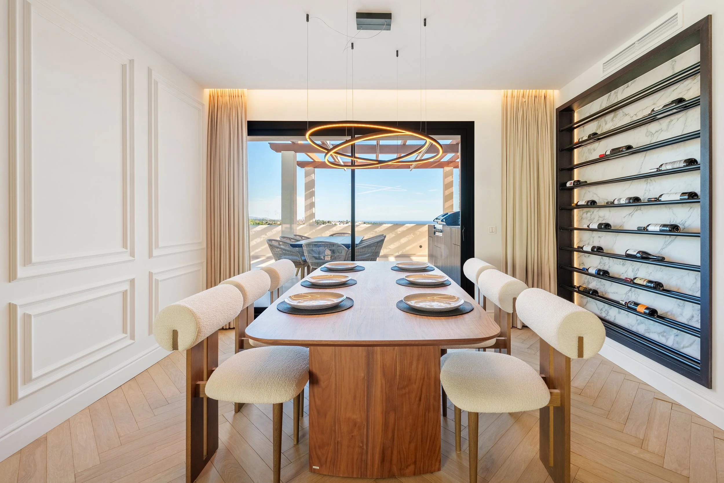 Elegant dining space with a natural wood table, designer lighting fixture, and a built-in floor-to-ceiling glass wine cellar.