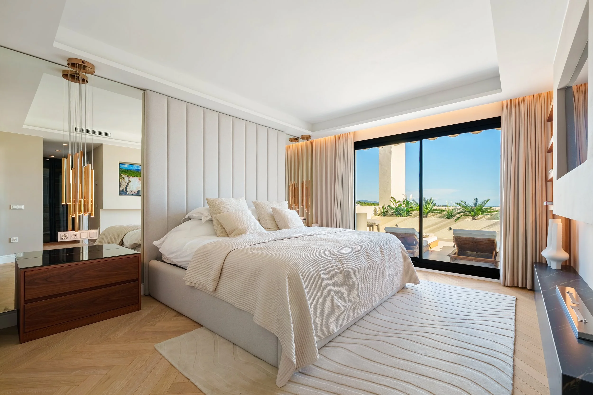 Sophisticated primary suite with a floor-to-ceiling upholstered headboard, neutral tones, and direct access to a private balcony.
