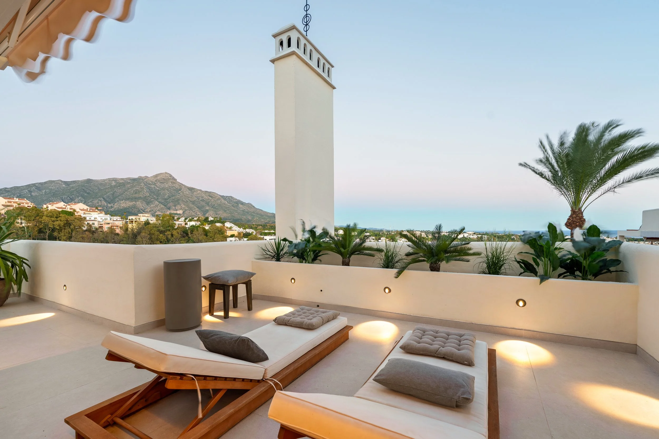 Sun-drenched terrace at sunset featuring luxury sun loungers and views of the sea, lake, and mountains.