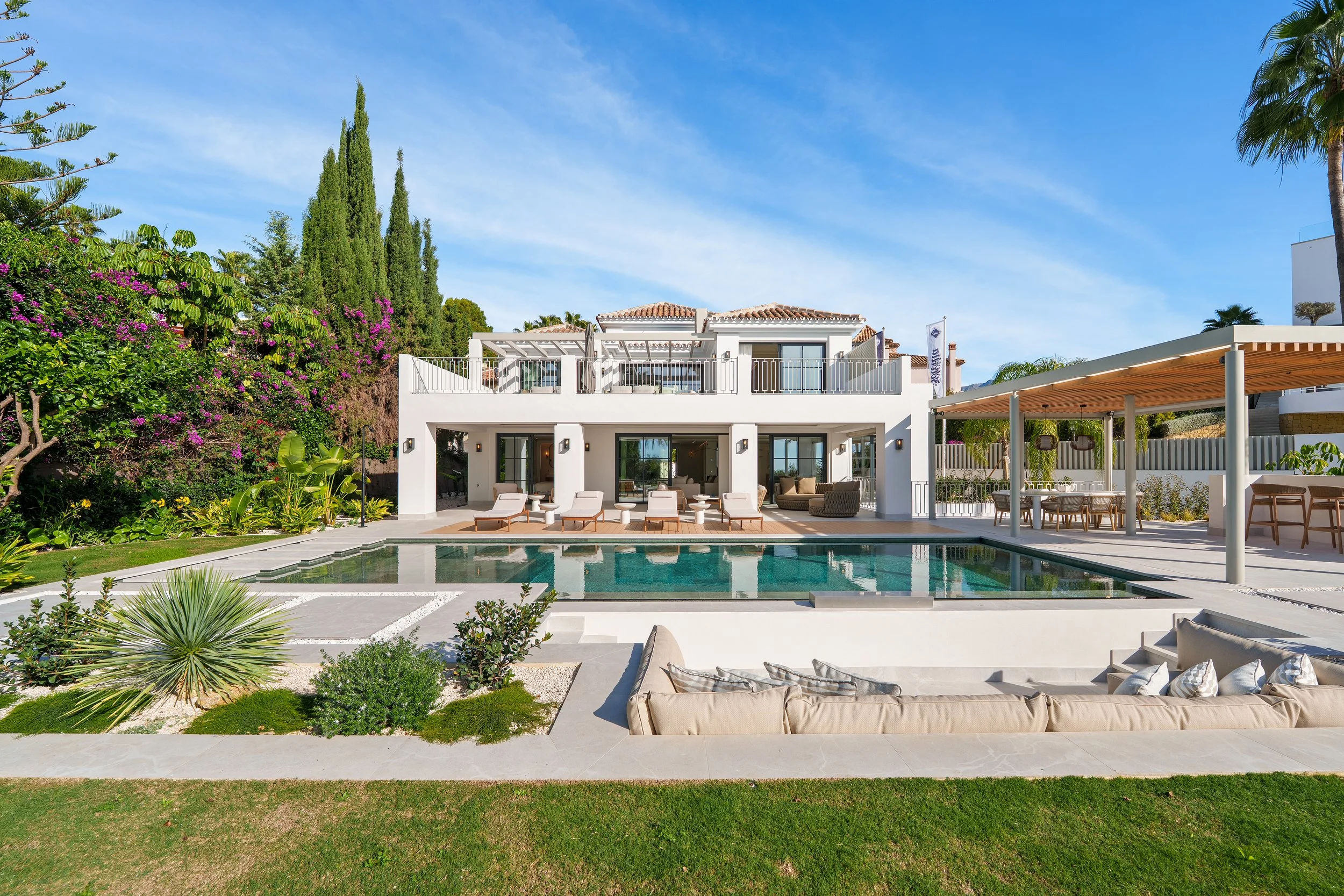 A breathtaking view of the newly renovated white Mediterranean villa, featuring clean lines, expansive glass doors, and a perfectly manicured lawn.