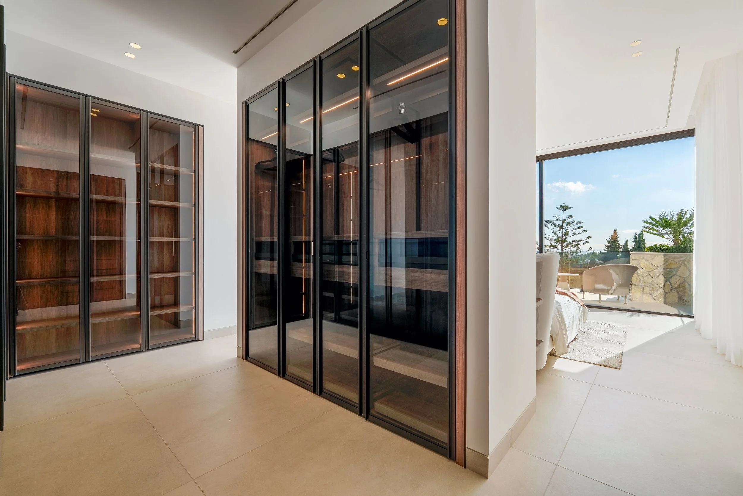 A spacious, walk-in master wardrobe with floor-to-ceiling smoked glass doors and integrated LED lighting